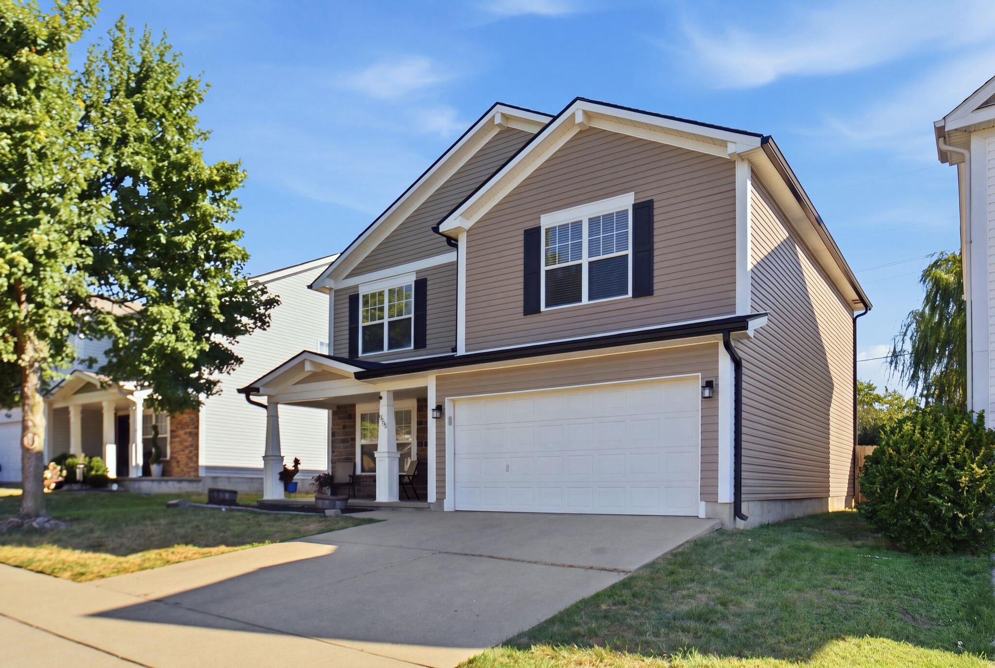 Two-story taupe house with a covered porch, black shutters, and a wide white garage door.
