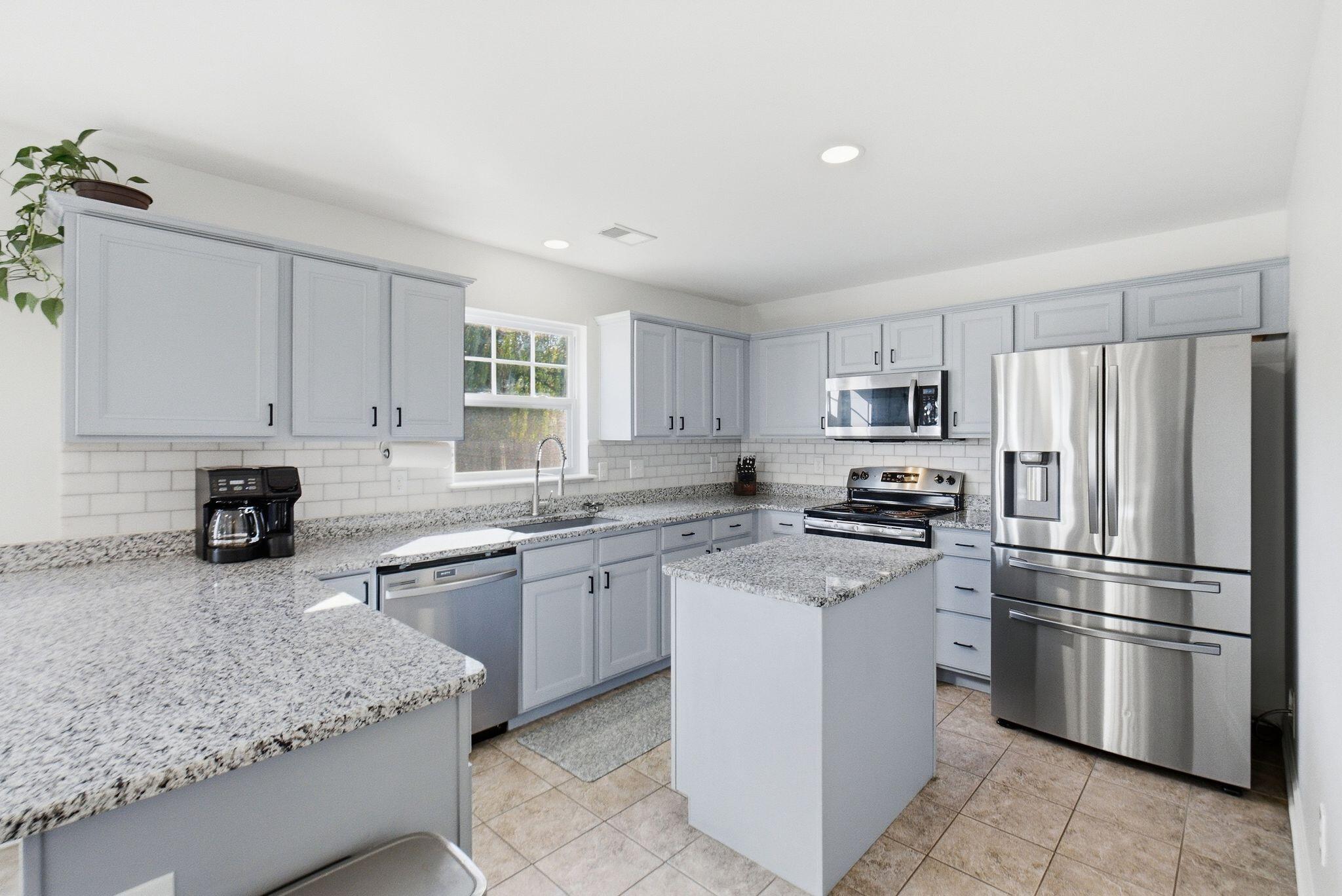 Kitchen with gray cabinets, granite counters, central island, and stainless steel appliances.