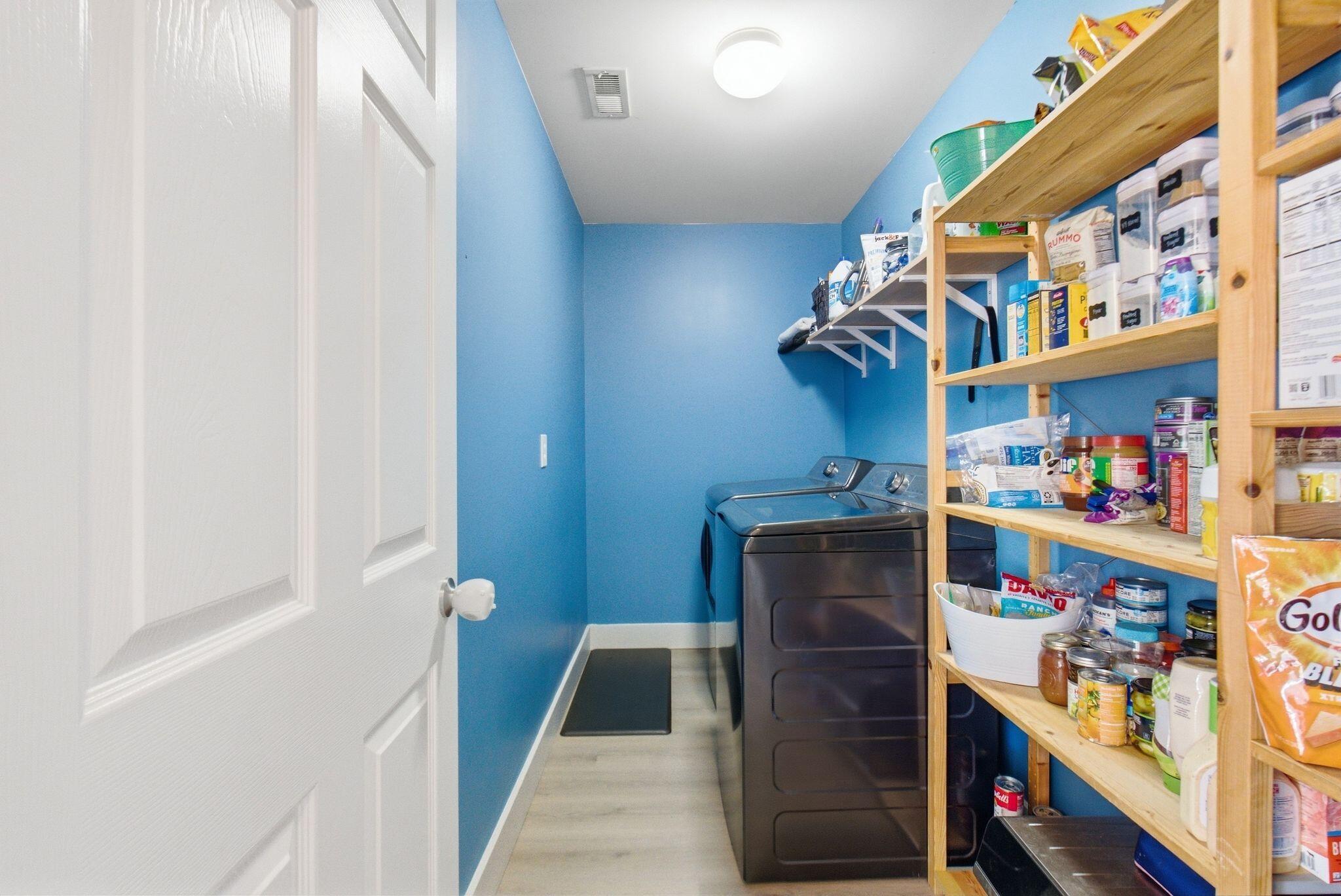 Laundry room with washer and dryer beside tall, stocked wooden shelving.