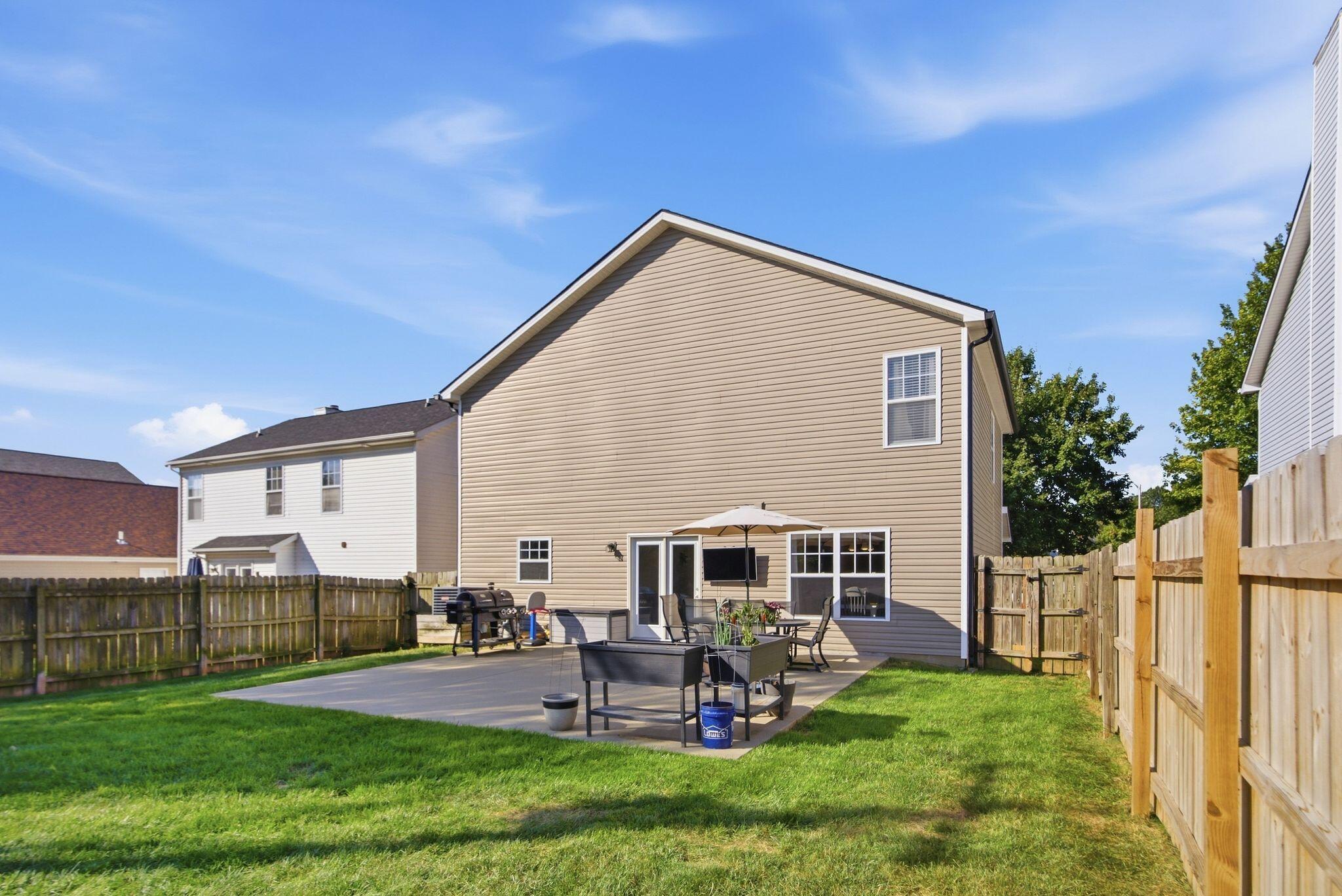 Home’s fenced backyard with a furnished concrete patio and umbrella.