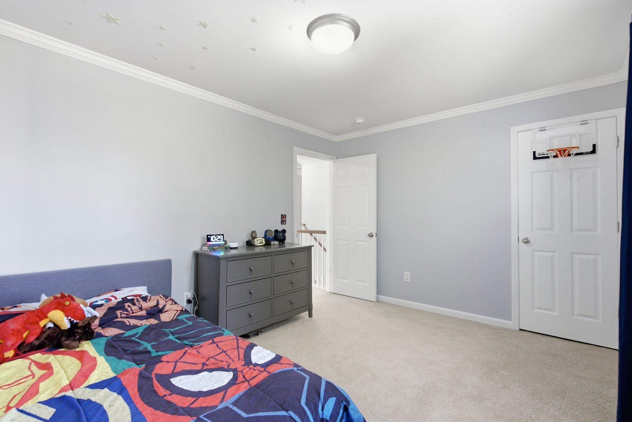Bedroom with colorful superhero bedding, a dresser, ceiling stars, and a basketball hoop on the door.