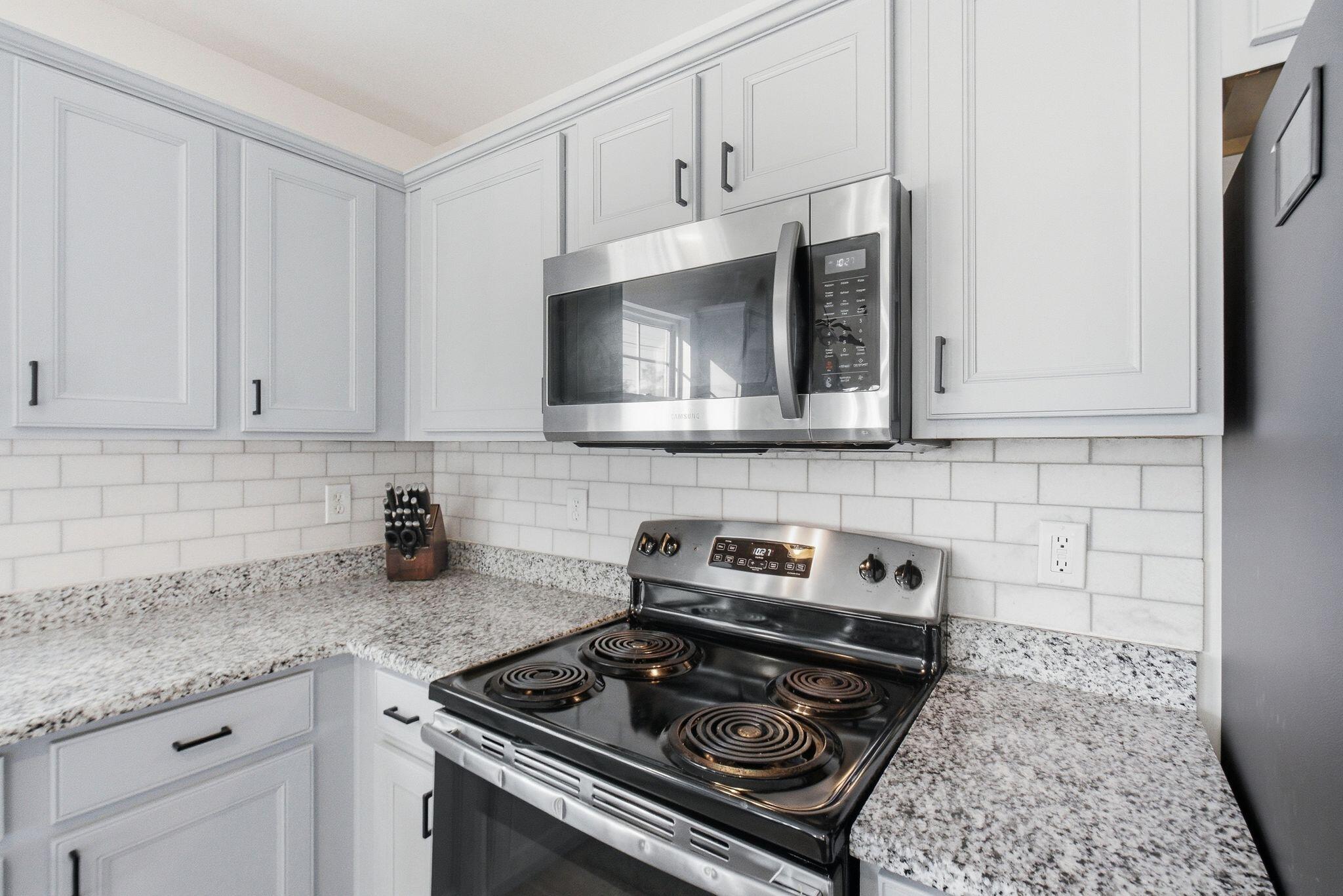 Kitchen with white shaker cabinets, granite countertops, subway-tile backsplash, and stainless-steel appliances.