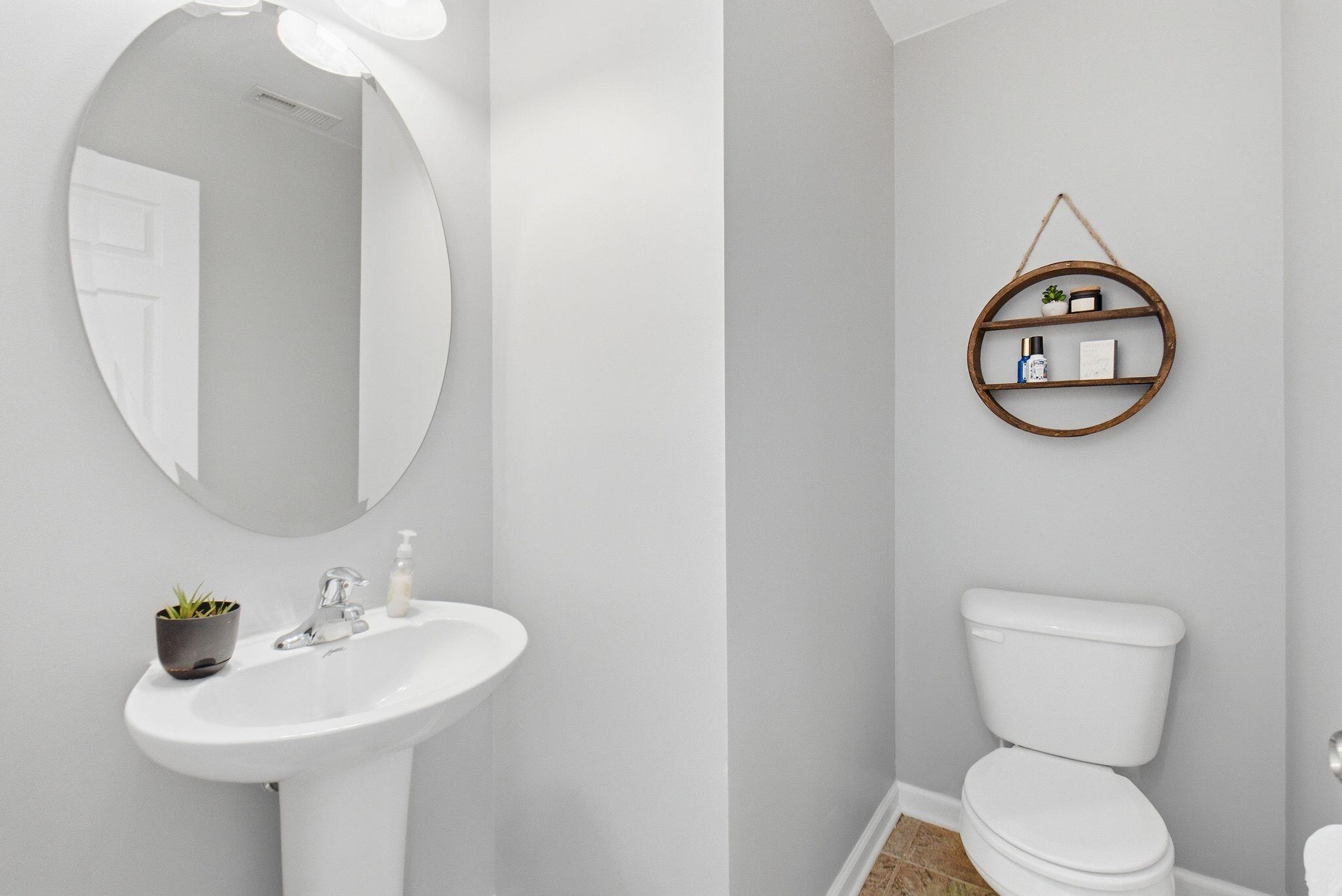 Bathroom with pedestal sink, oval mirror, toilet, and round wooden wall shelf.