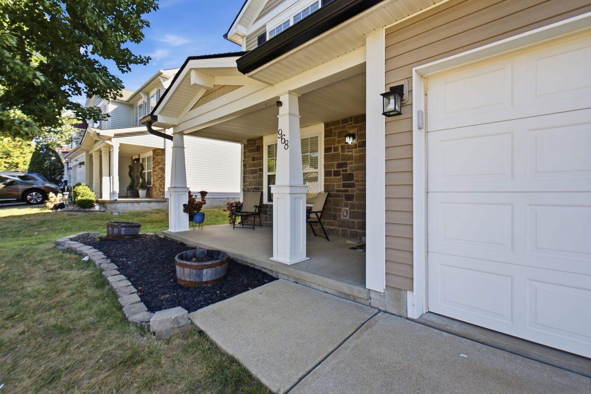 Home exterior with a stone-accented covered porch, white garage door, and landscaped front bed.