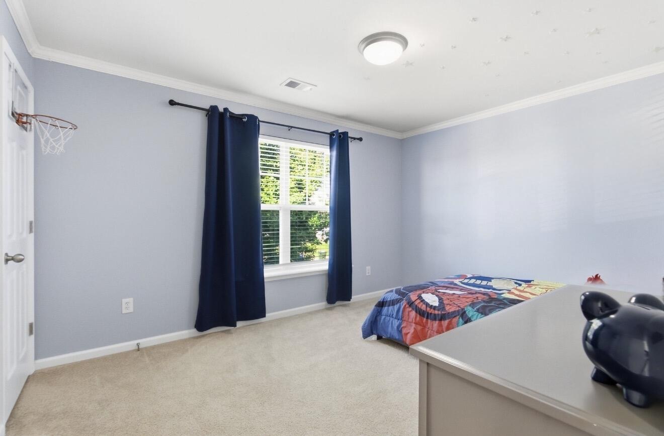 Bedroom with pale blue walls, navy curtains, colorful bedding, and a basketball hoop on the door.