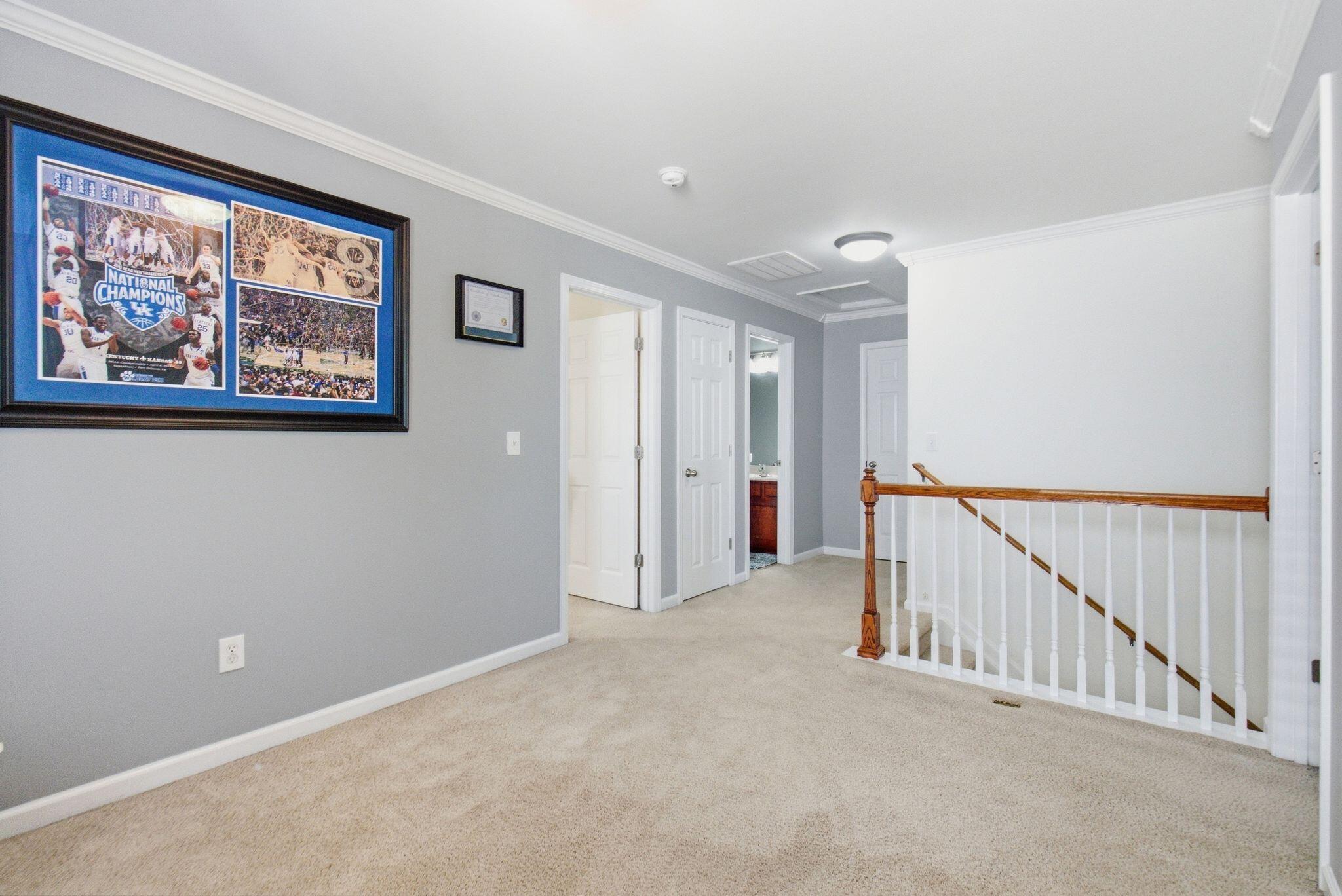 Carpeted upstairs landing with a framed basketball championship collage and wooden stair railing.