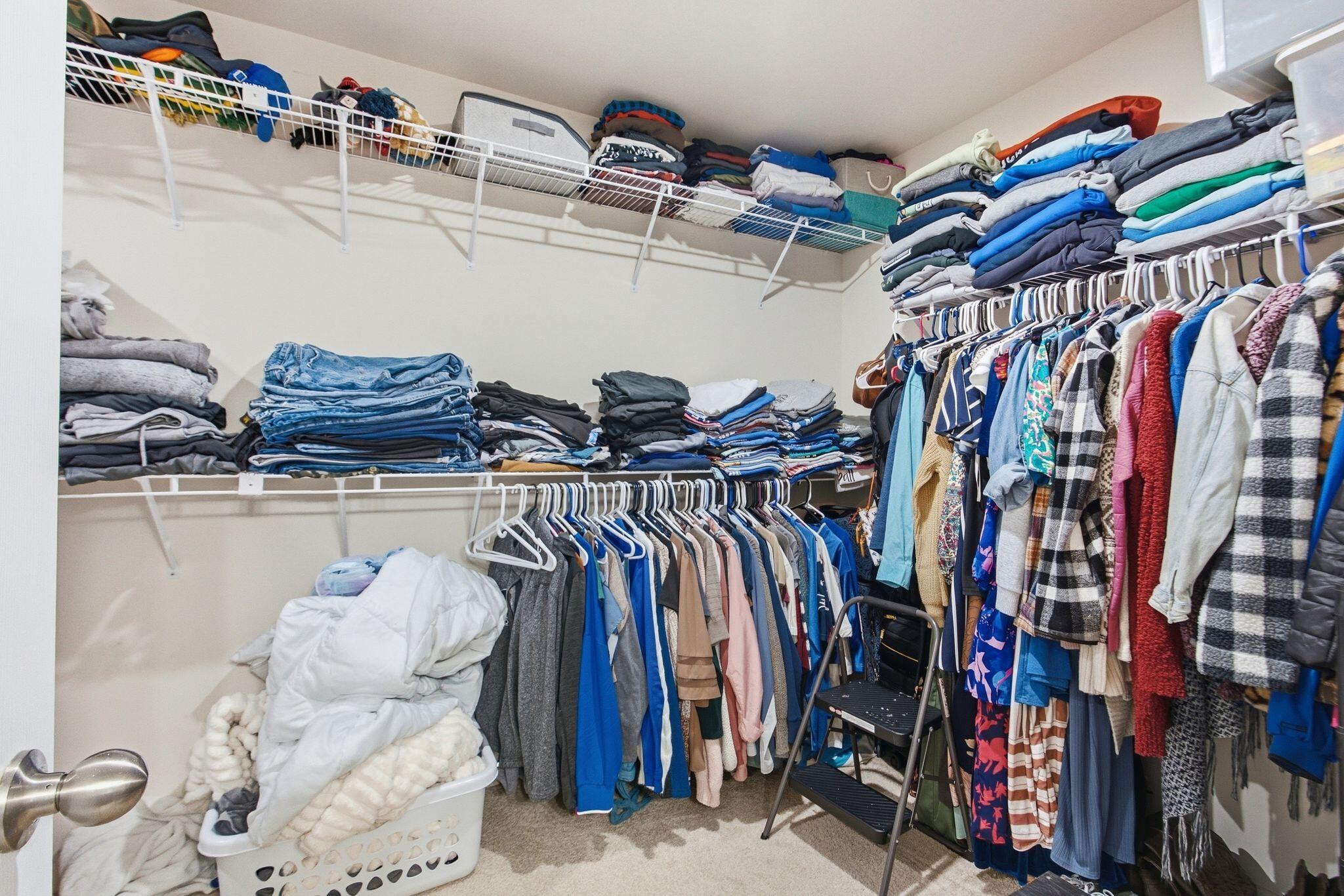 Walk-in closet with extensive wire shelving, folded clothes, hanging garments, and a laundry basket.