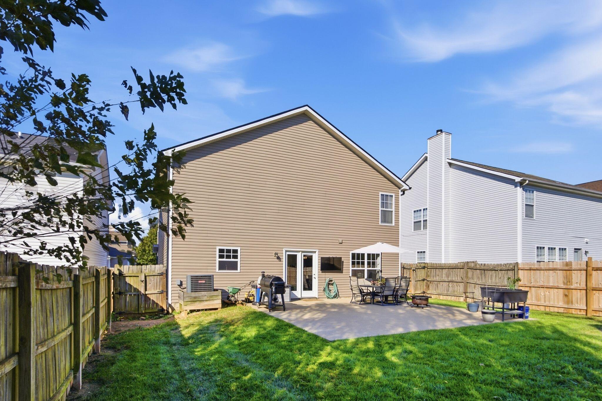 Backyard patio with outdoor dining set and grill beside a fenced lawn.