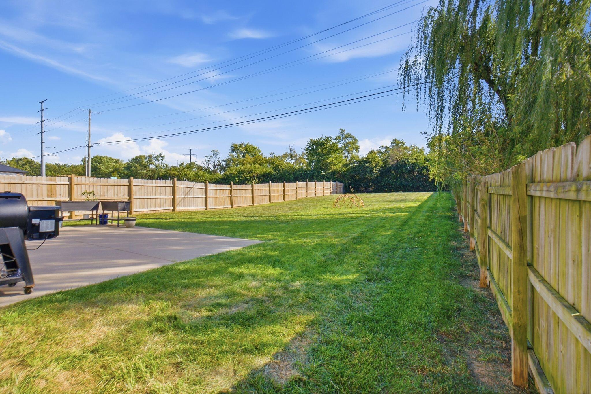 Fenced backyard with a broad lawn, concrete patio, and outdoor grill.