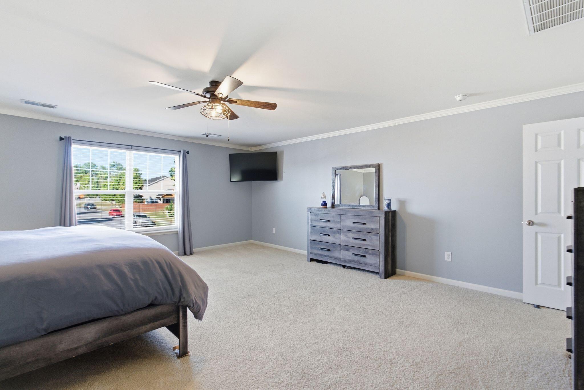 Bedroom with gray bedding, a wide window, ceiling fan, and gray dresser with mirror.
