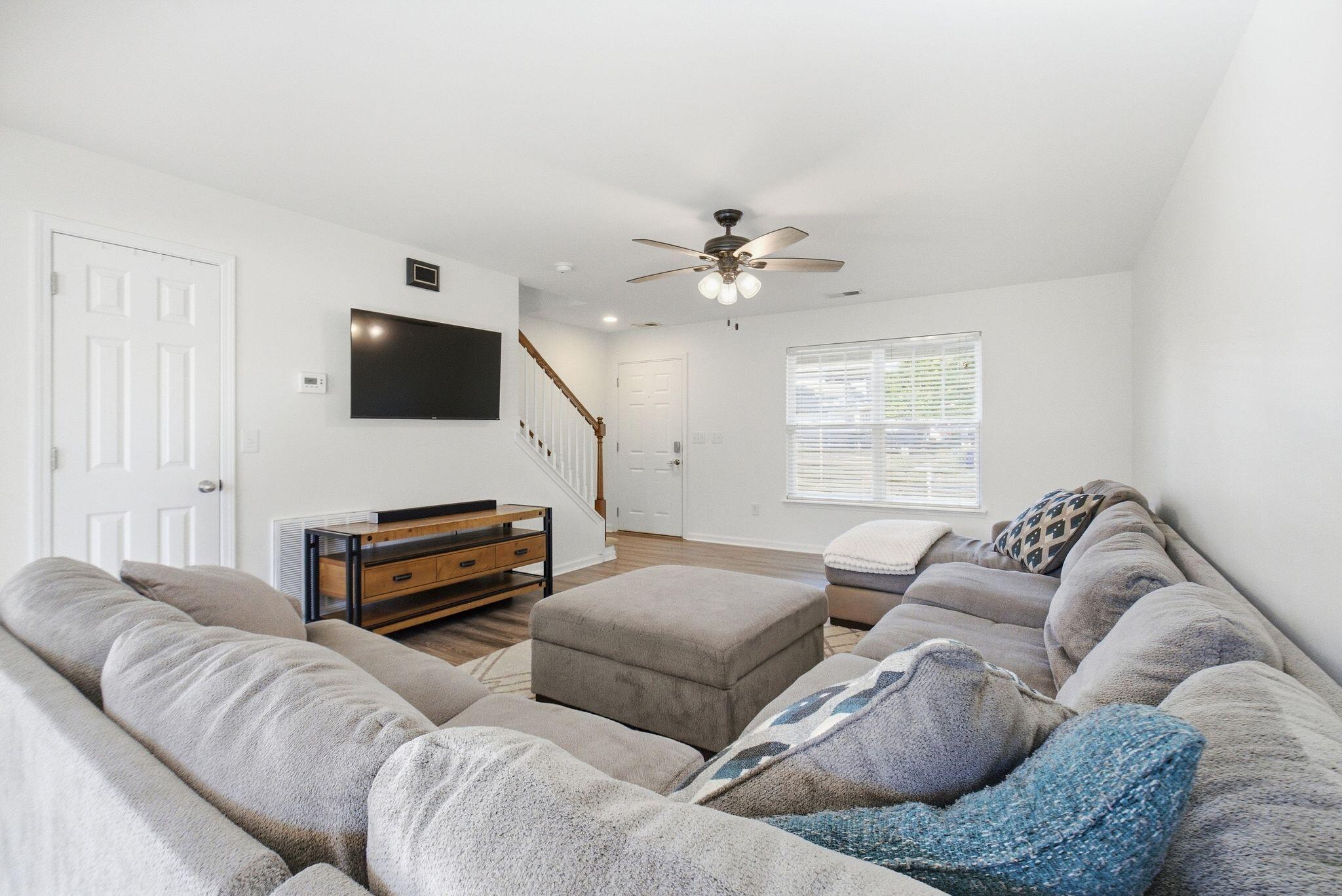 Furnished living room with a large gray sectional, ottoman, wall-mounted TV, and staircase.