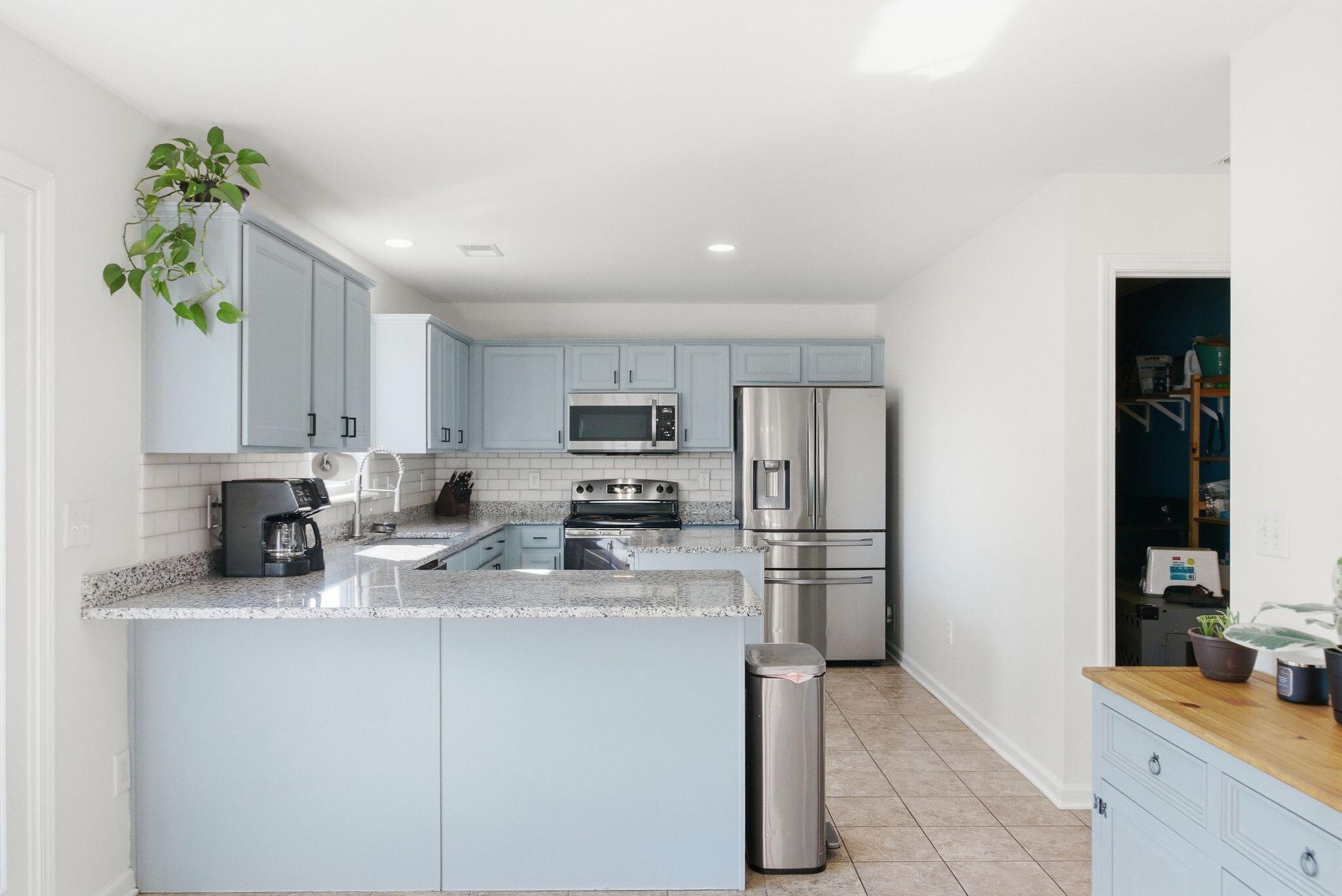 Kitchen with pale blue cabinets, granite peninsula, subway tile backsplash, and stainless steel appliances.
