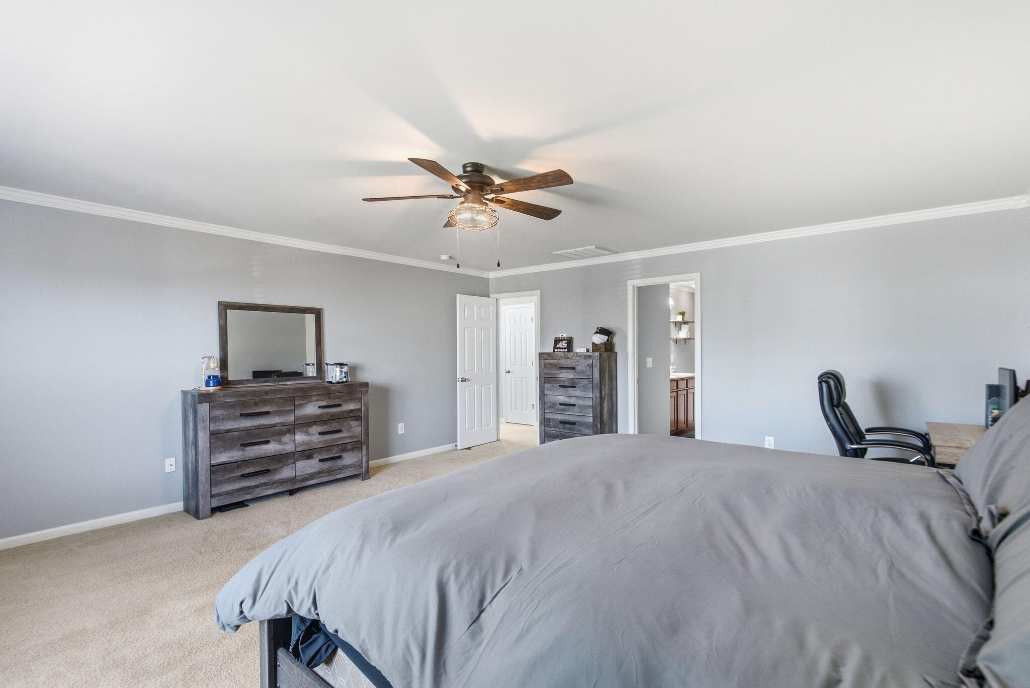 Bedroom with gray bedding, a dark wood dresser and mirror, and a ceiling fan with light.