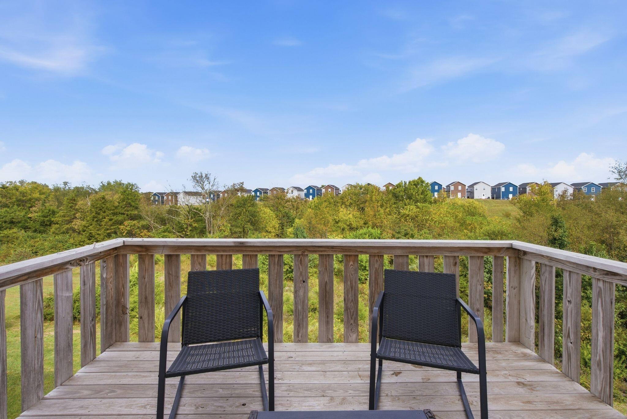Wooden deck with two black chairs overlooking wooded greenery and neighboring homes.