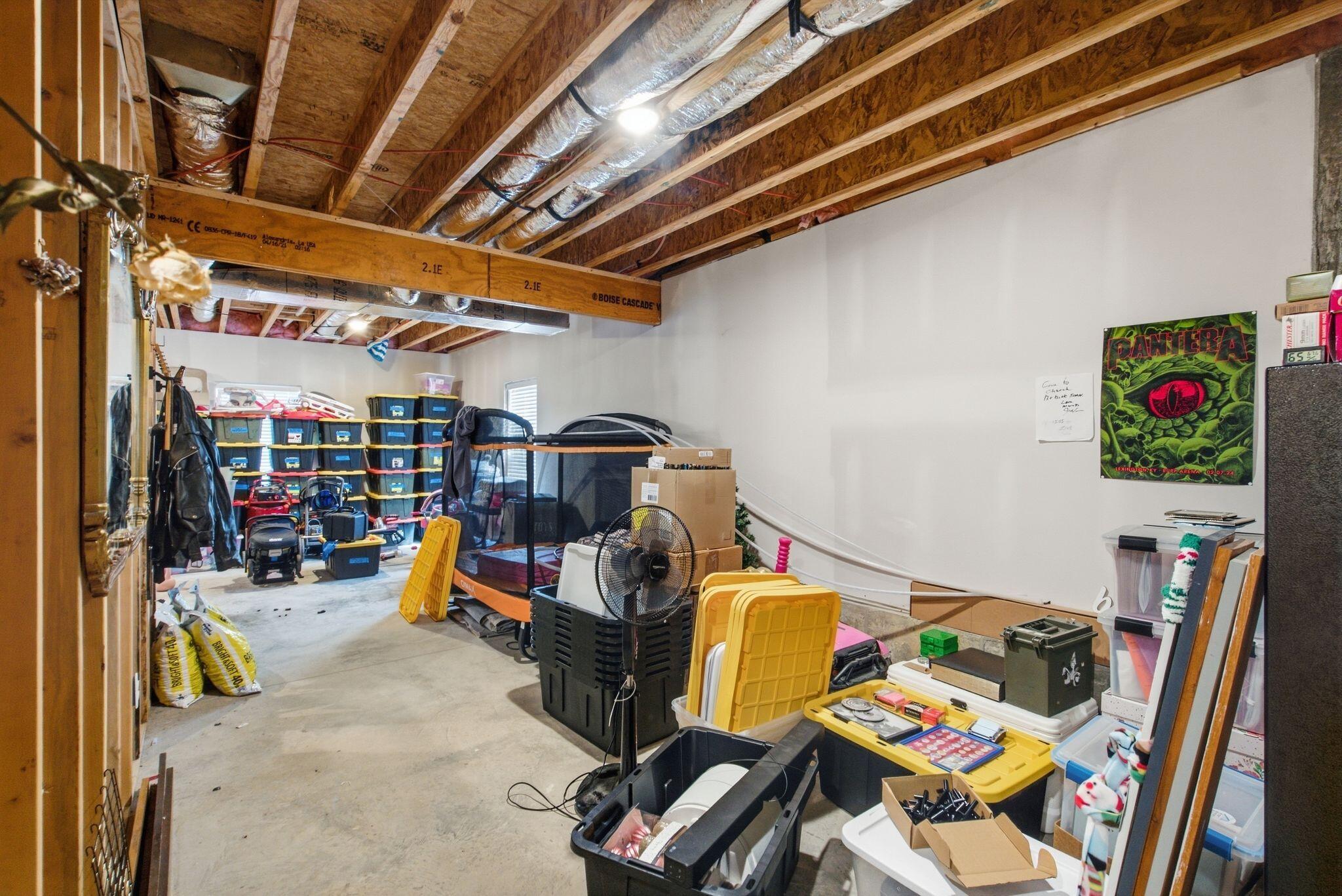 Unfinished basement storage area with exposed ceiling joists, ductwork, and stacked bins.
