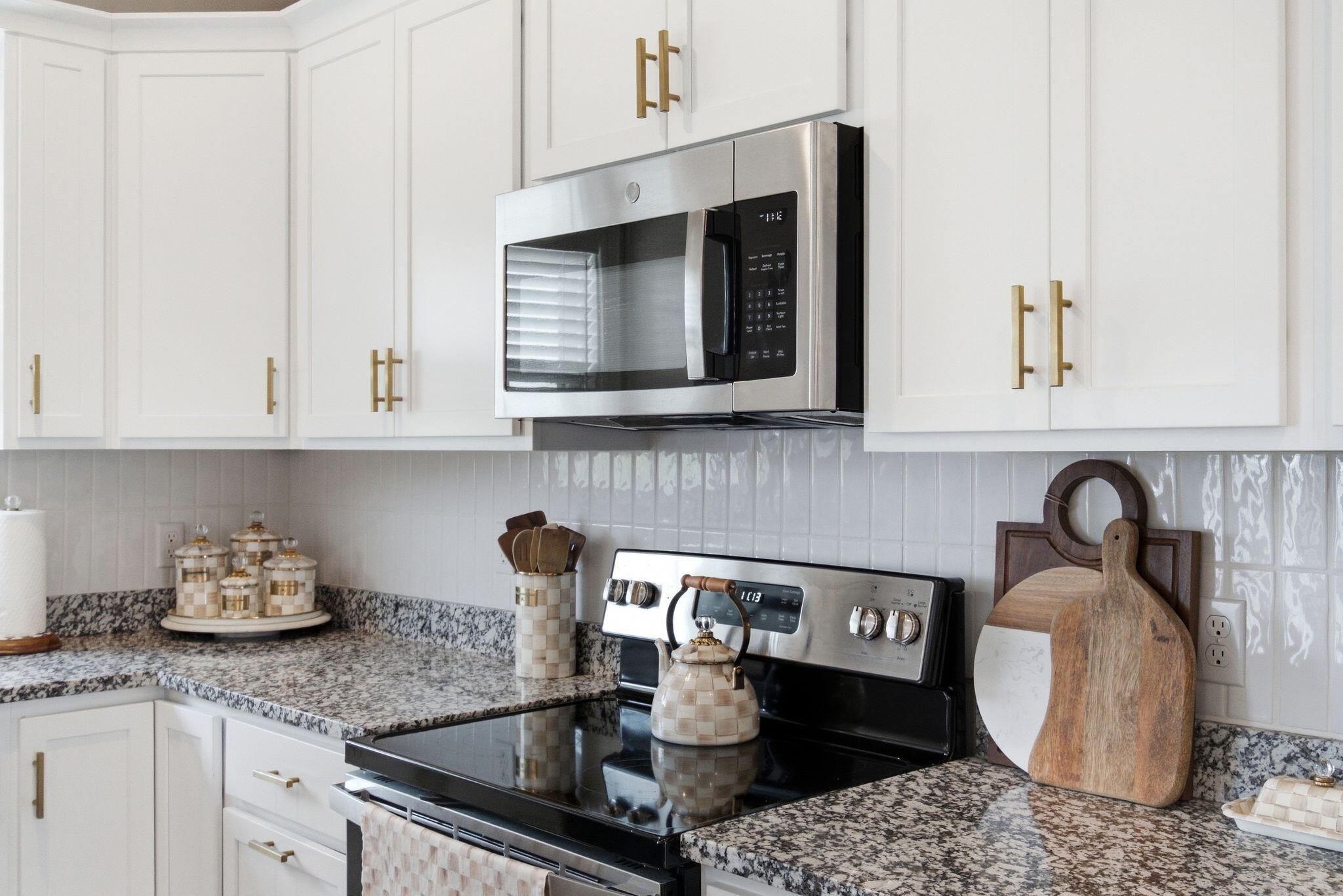 Kitchen with white shaker cabinets, granite counters, and a stainless microwave above a black range.