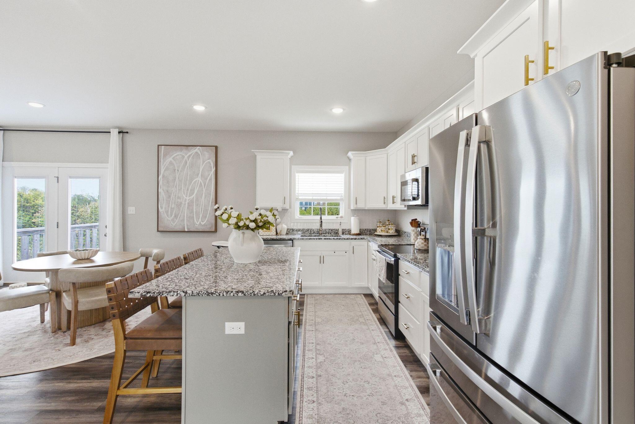 Bright kitchen with a granite island, white cabinets, and stainless steel appliances.