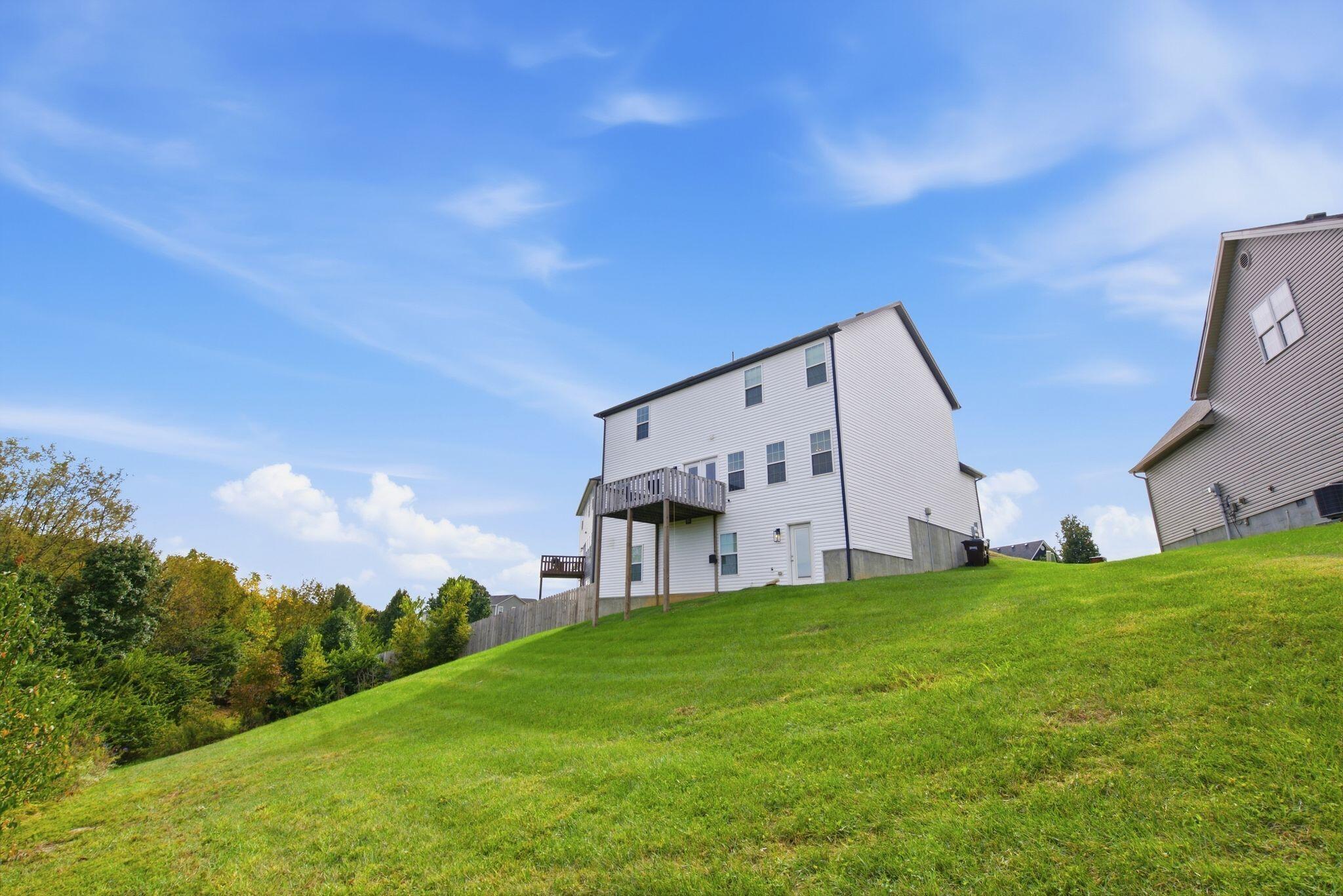 Rear of a two-story white-sided home with a raised deck above a sloping lawn.