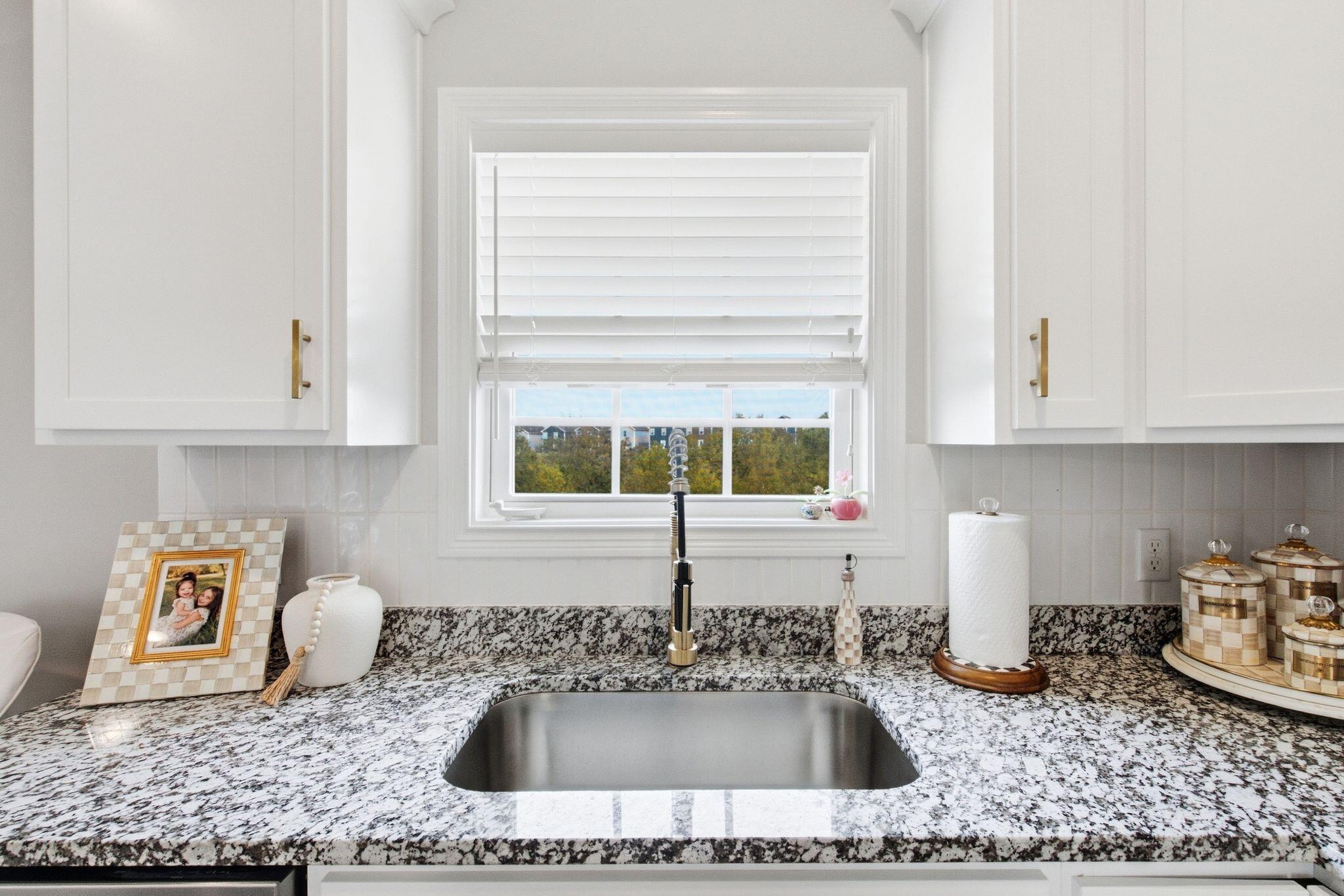 Kitchen sink and speckled granite countertop beneath a window with white blinds.