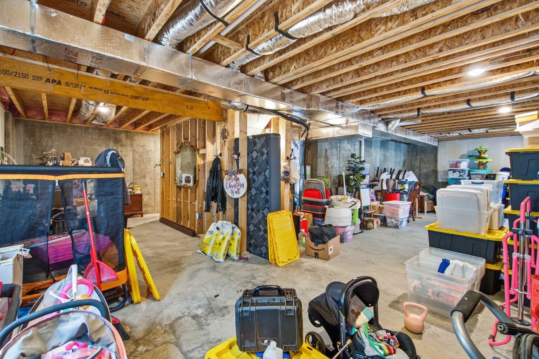 Unfinished basement with exposed ceiling joists, ductwork, concrete walls, and stored household items.