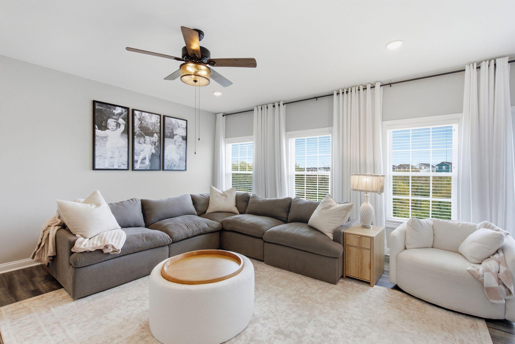 Living room with a gray sectional, white accent chair, and large curtained windows.