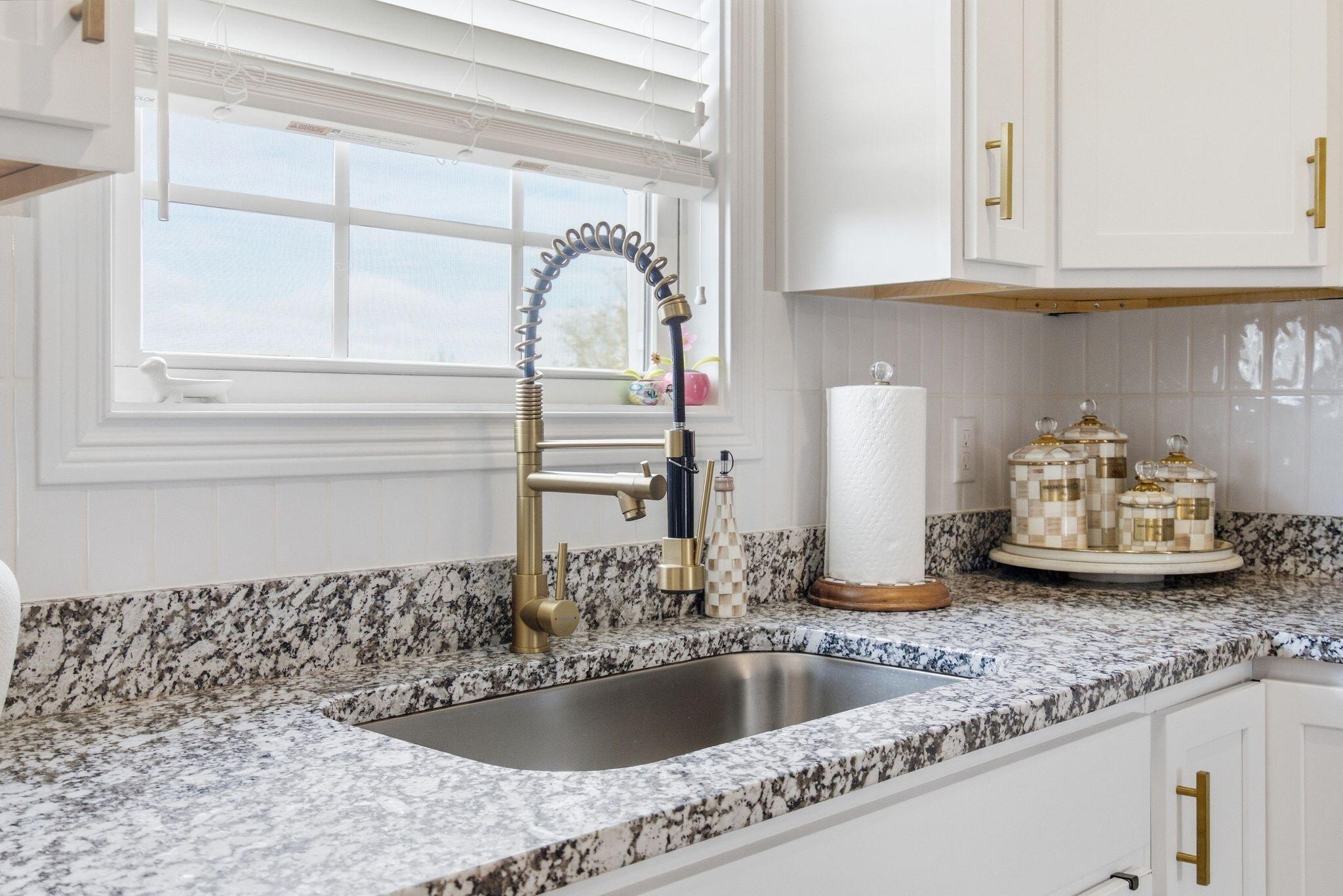 Kitchen sink beneath a window, with a gold-tone faucet and speckled granite countertops.