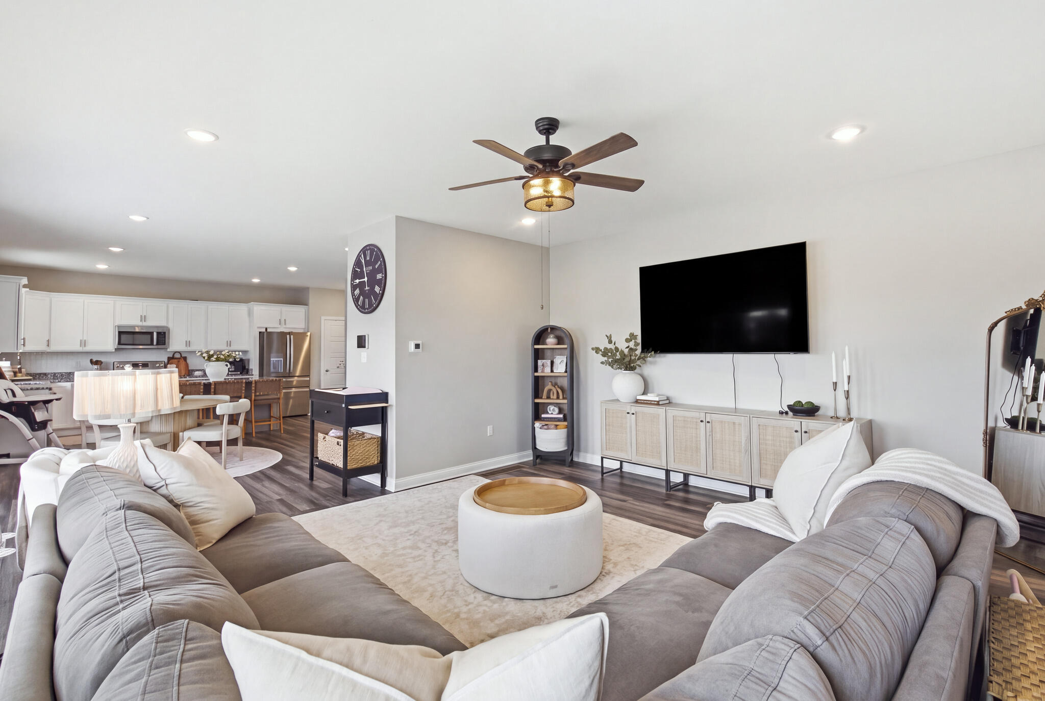 Open-plan living room with gray sofas, a wall-mounted TV, and the kitchen beyond.