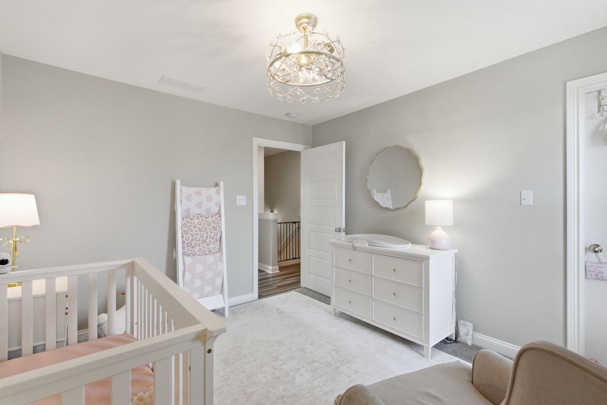 Nursery with a white crib, changing dresser, round mirror, and crystal chandelier.