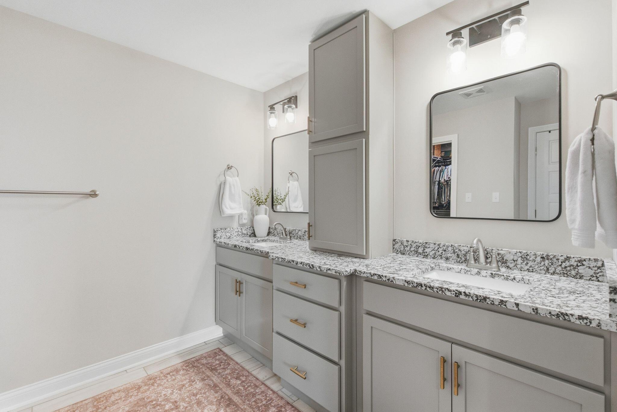 Bathroom with twin sinks, gray cabinets, patterned stone counters, and large framed mirrors.