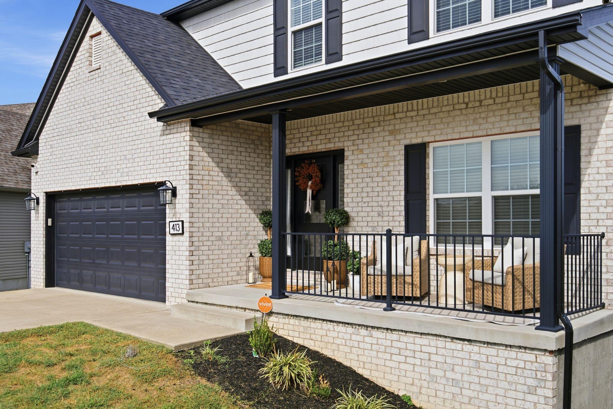 Brick home exterior with covered porch, dark garage door, and wicker seating.