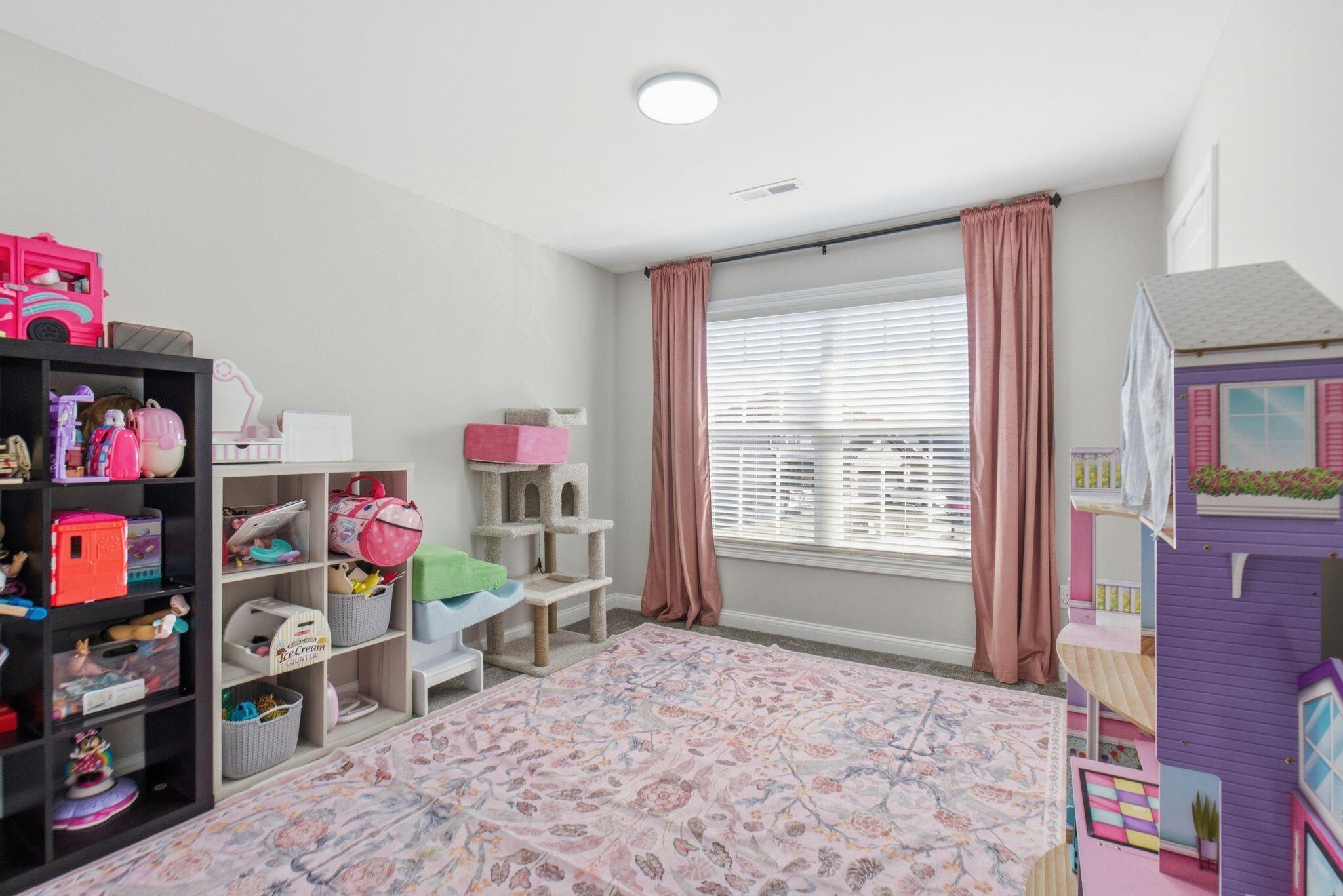Playroom with a large window, pink curtains, toy shelves, a cat tree, and a dollhouse.