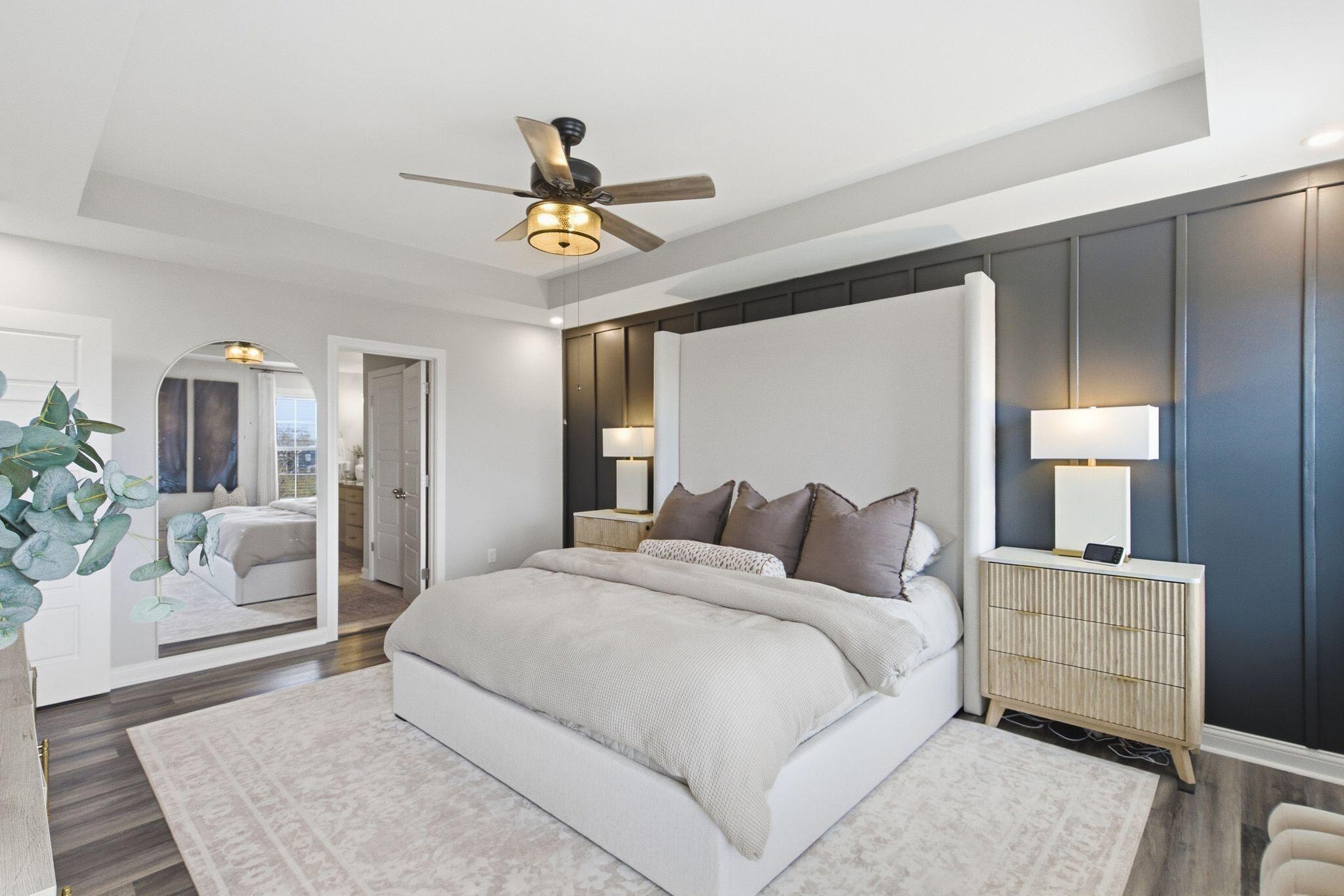 Staged bedroom with a white bed, dark paneled accent wall, and ceiling fan.