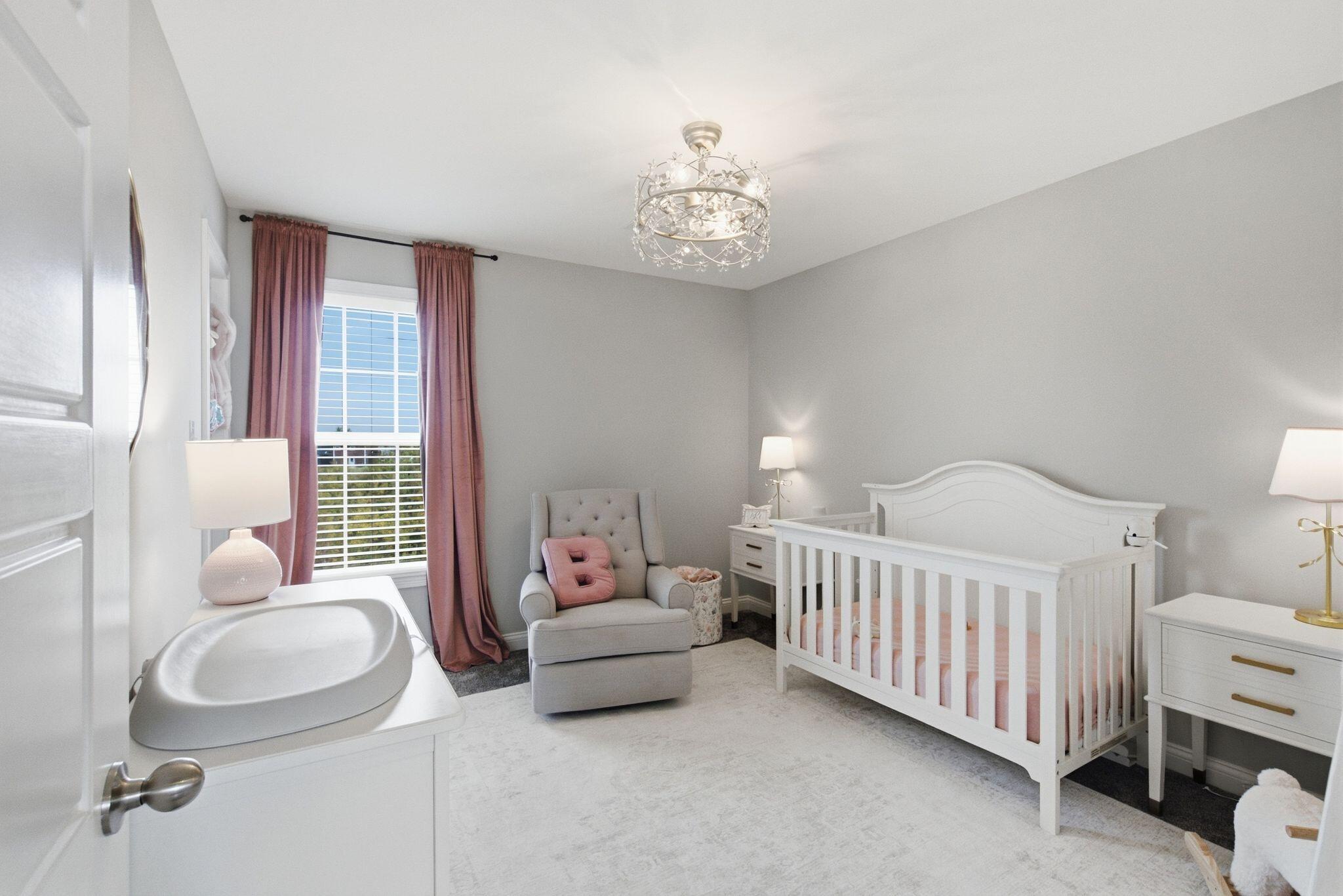 Nursery with a white crib, pink curtains, and a tufted gray glider.