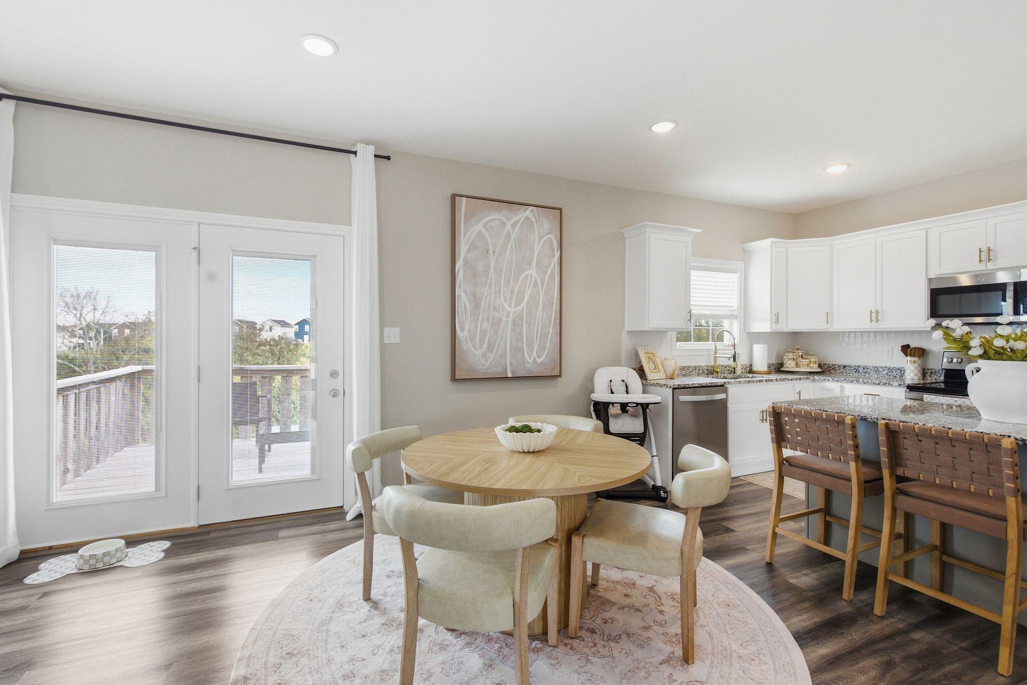 Open kitchen and dining area with white cabinets, granite island, and round wood table by patio doors.
