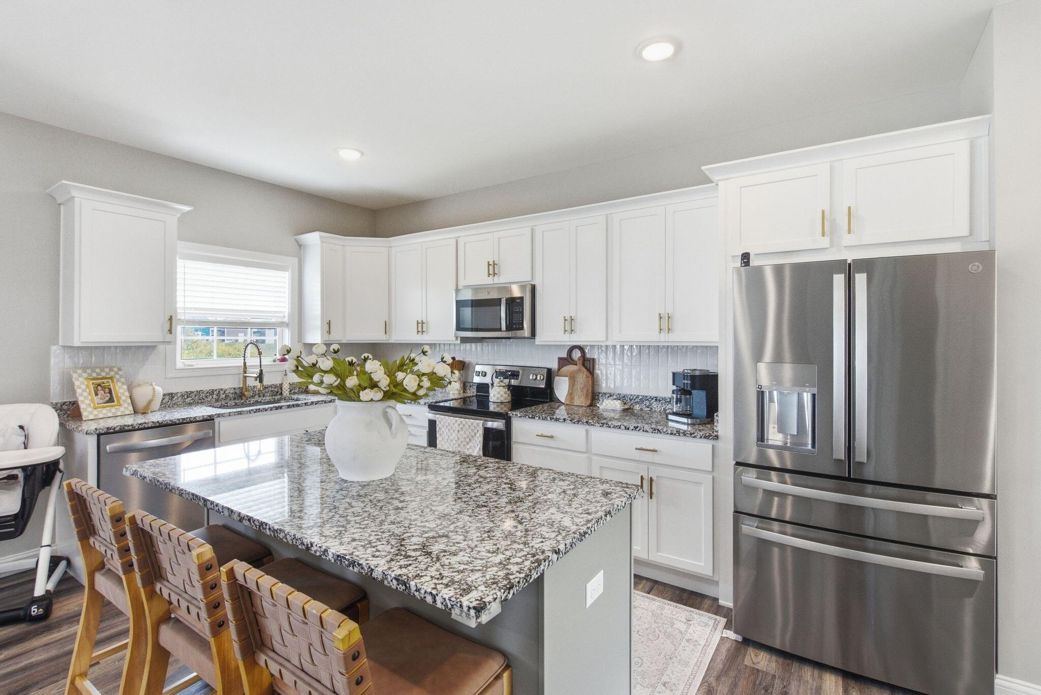 Bright kitchen with white cabinets, granite island, bar stools, and stainless steel appliances.
