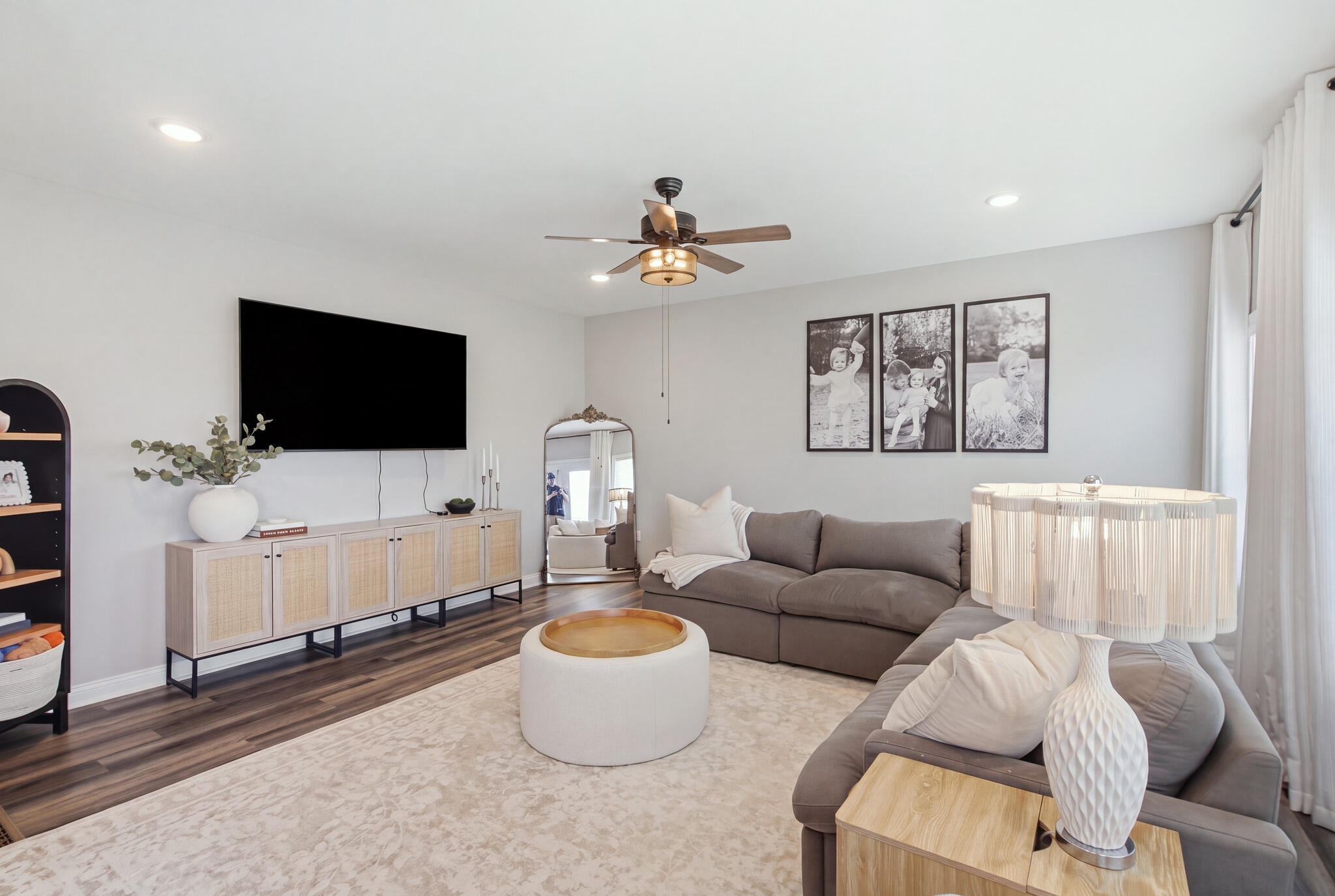 Living room with gray sectional, wall-mounted TV, and a ceiling fan with light.