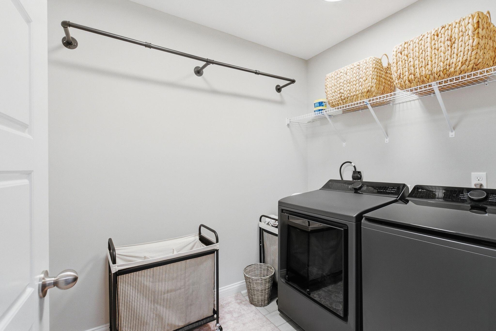 Laundry room with dark washer and dryer, woven baskets, and a hanging rod.