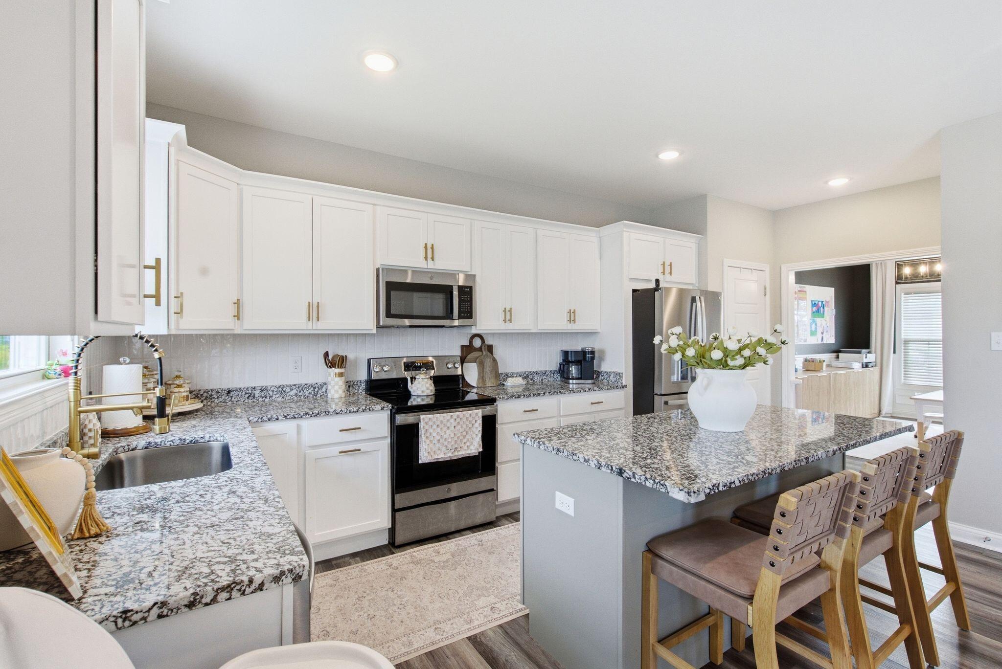Bright kitchen with white cabinets, granite counters, stainless appliances, and a large island with seating.
