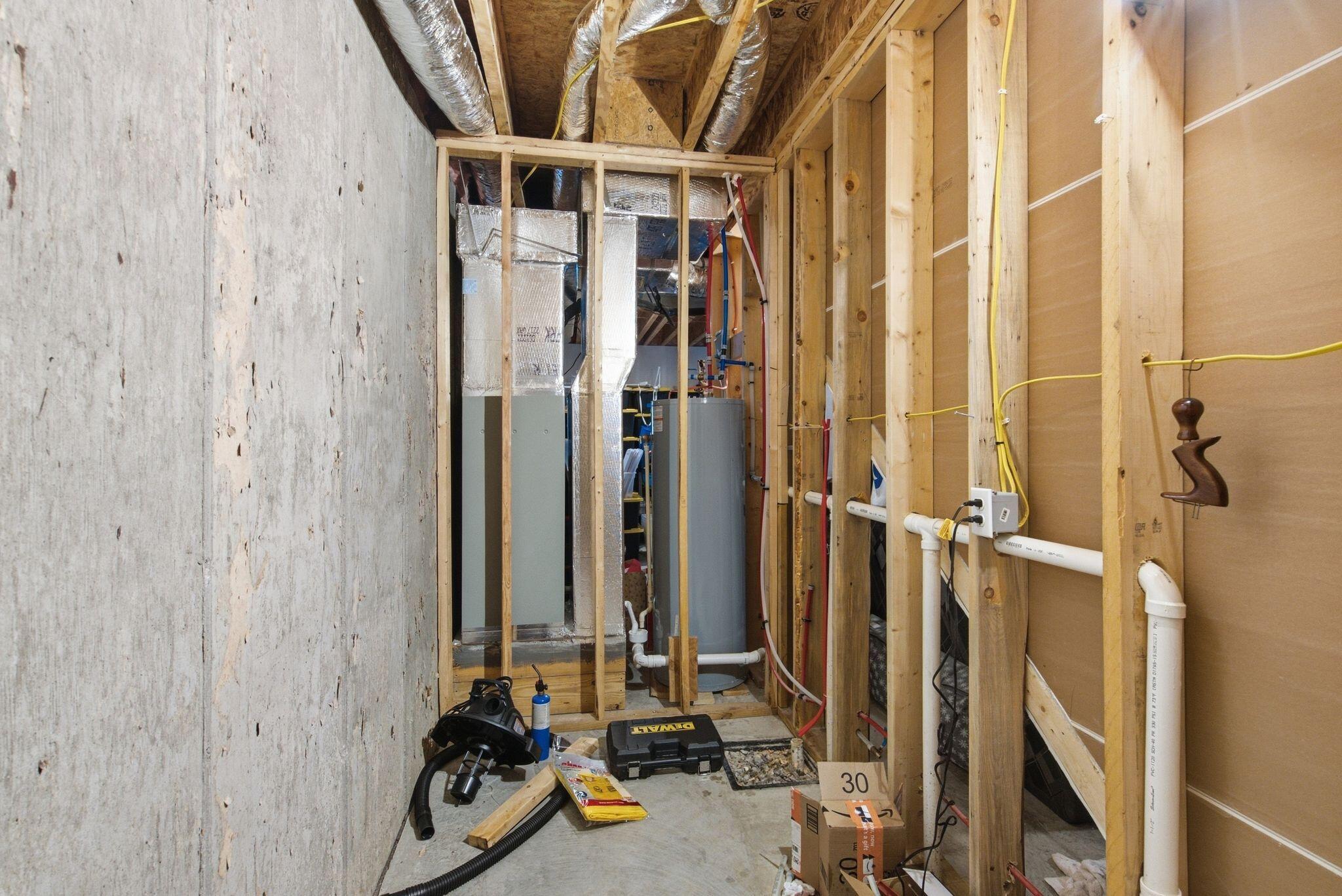 Unfinished utility room with exposed framing, HVAC ducts, plumbing, and a water heater.