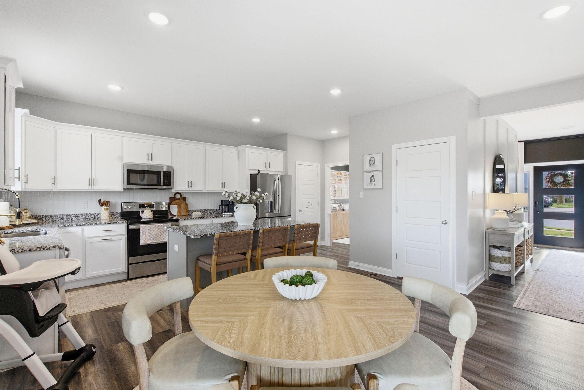 Bright kitchen with white cabinets, granite island, stainless appliances, and a round dining table.