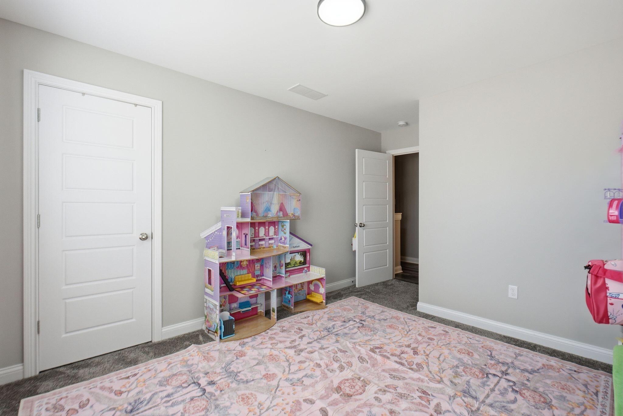 Bedroom with a colorful dollhouse, patterned rug, and gray carpet.
