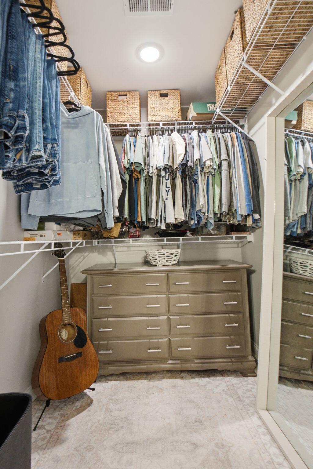 Walk-in closet with hanging clothes, woven storage baskets, a dresser, and an acoustic guitar.
