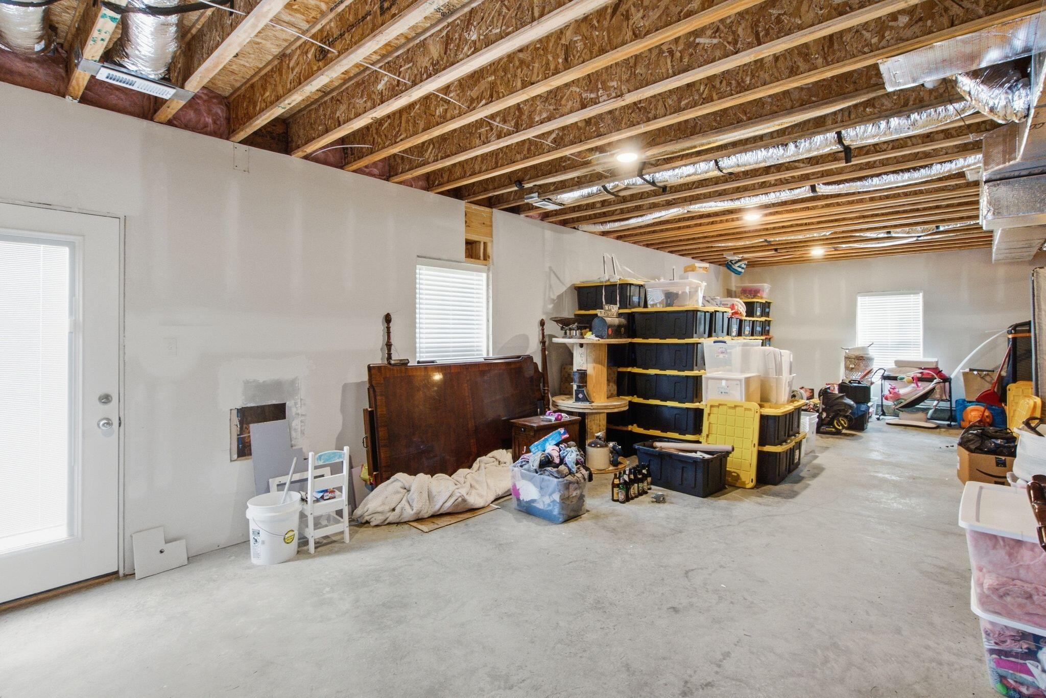 Garage with exposed ceiling joists, concrete floor, and stacked storage bins.