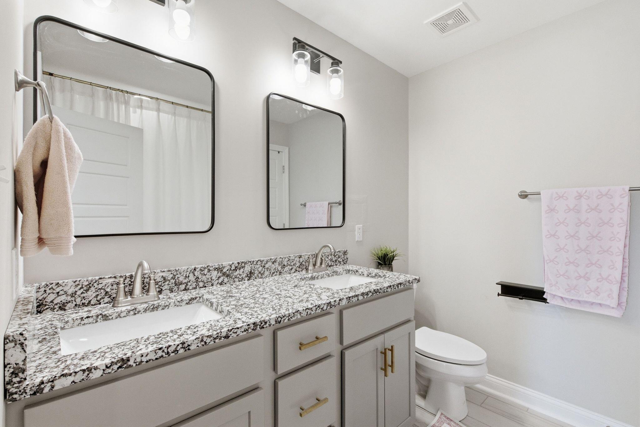 Bathroom with a double-sink granite vanity, black-framed mirrors, and a toilet.