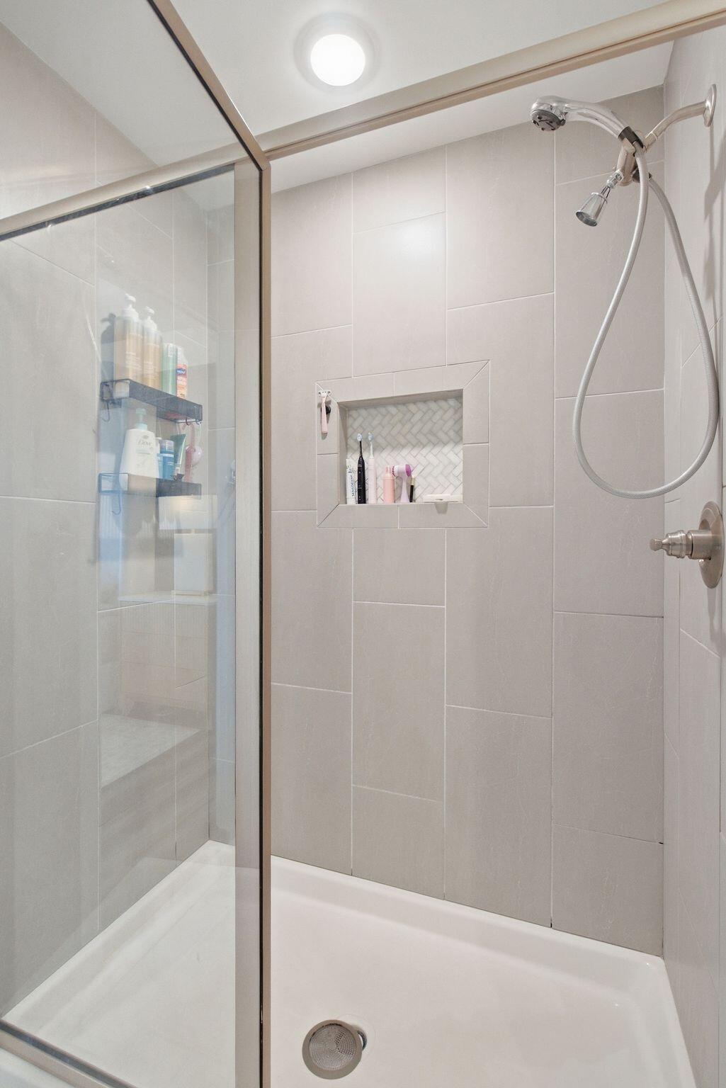Walk-in shower with a glass enclosure, large gray tiles, and a herringbone niche.