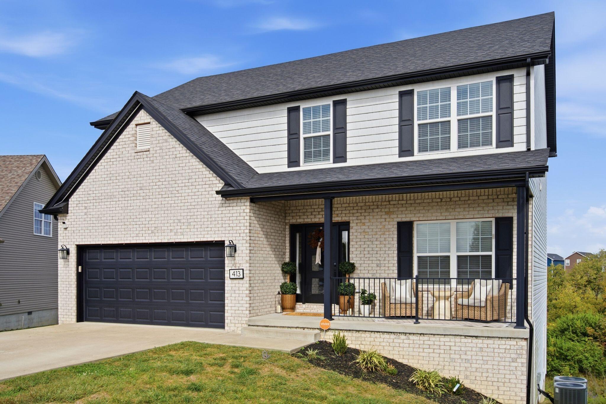Two-story brick-and-siding home with a dark garage door and furnished covered porch.