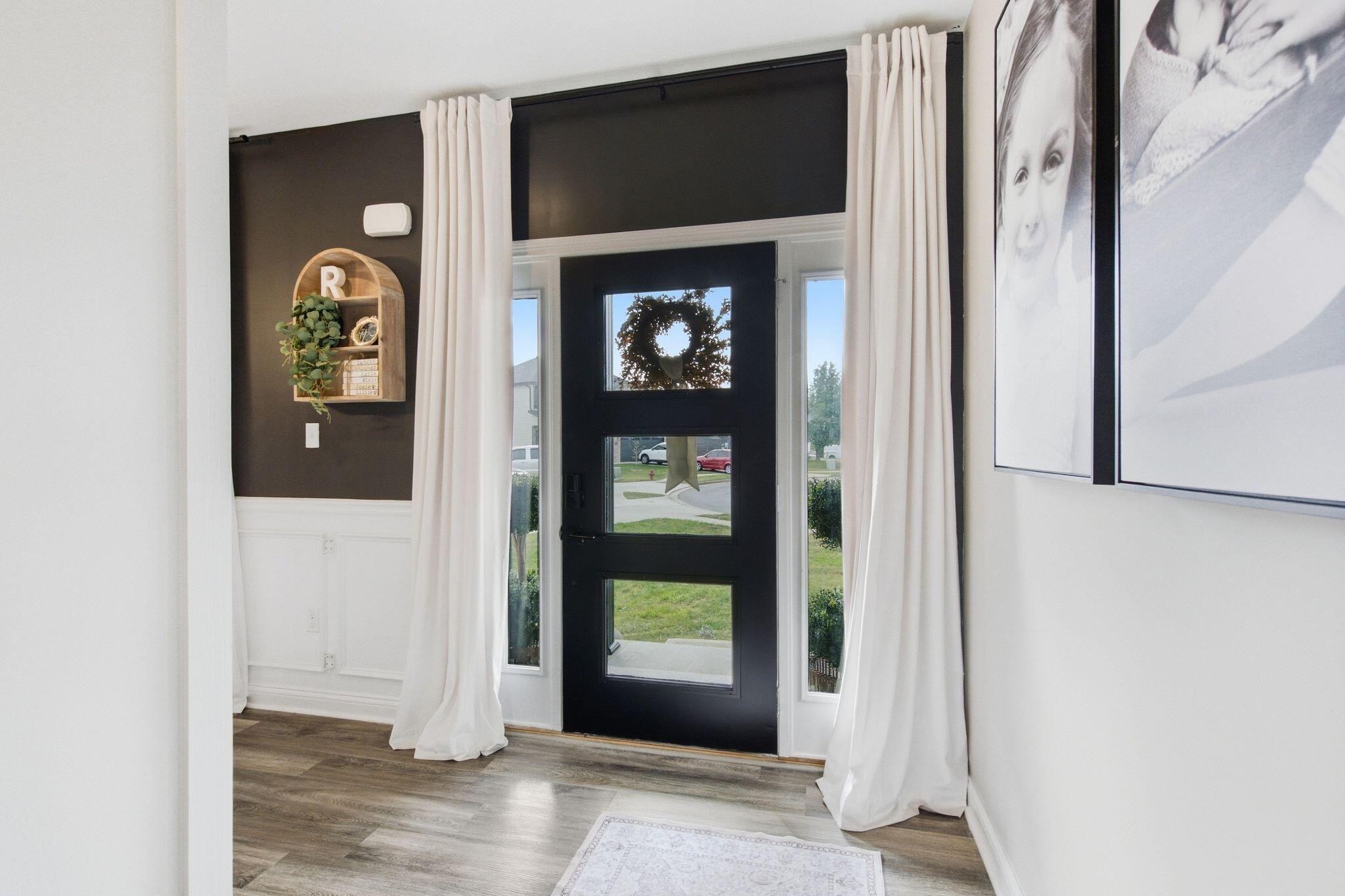 Entry foyer with a black glass-paneled front door, white curtains, and dark accent wall.