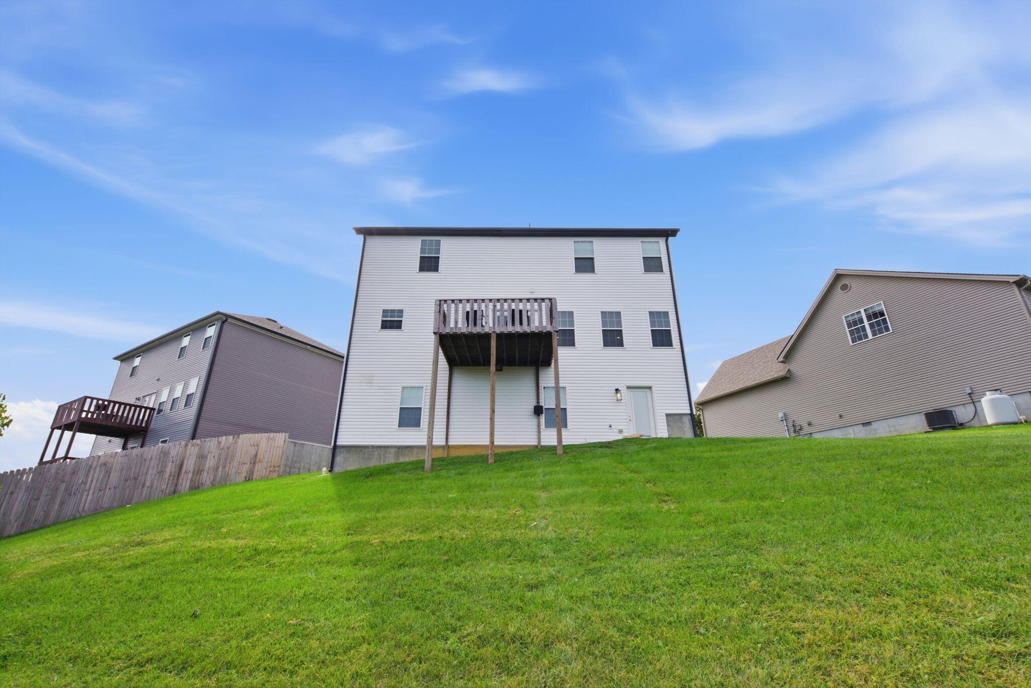 Rear of a three-story white-sided home with a raised deck overlooking a sloped lawn.