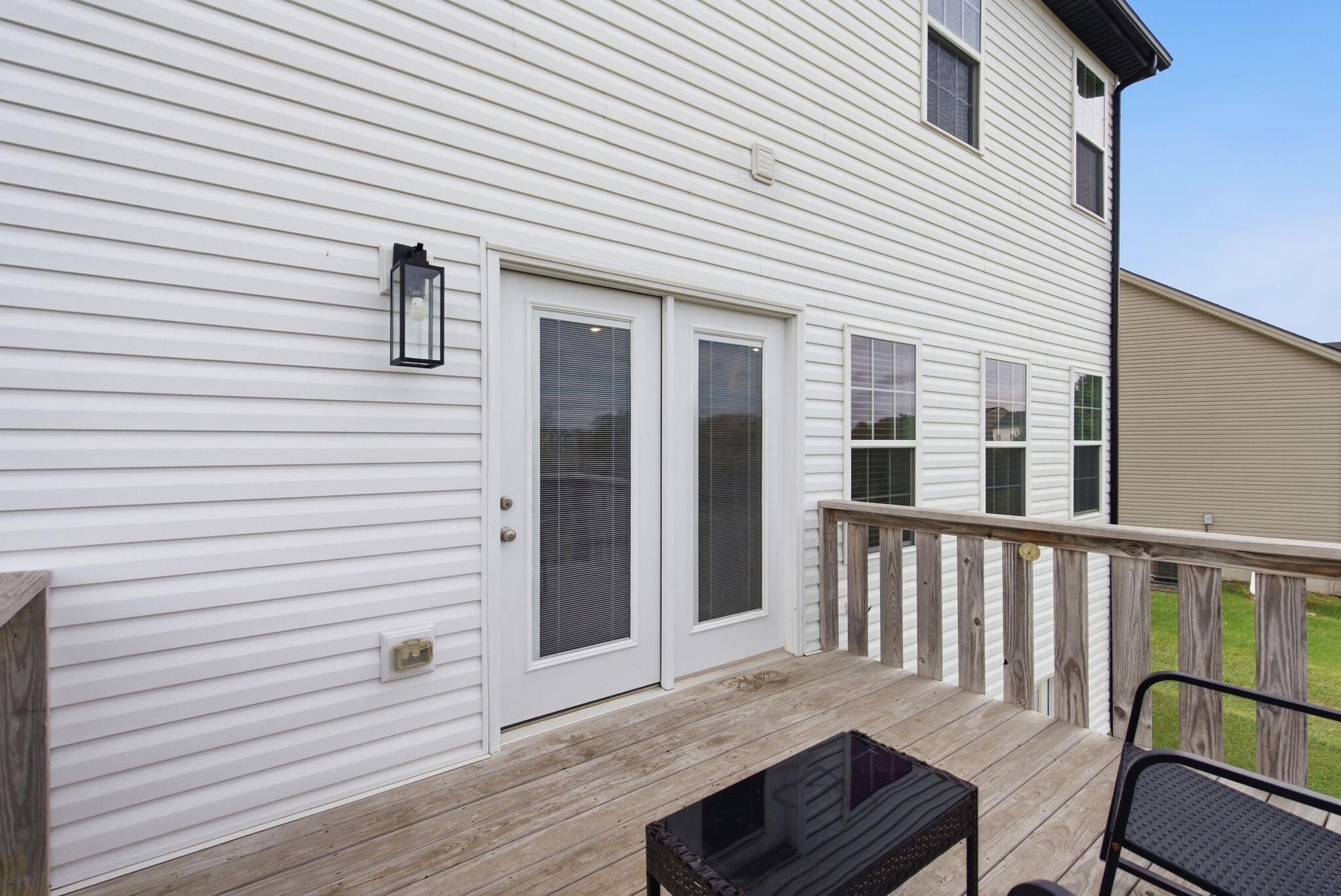 Rear deck with white siding, double glass doors, wooden railing, and outdoor seating.