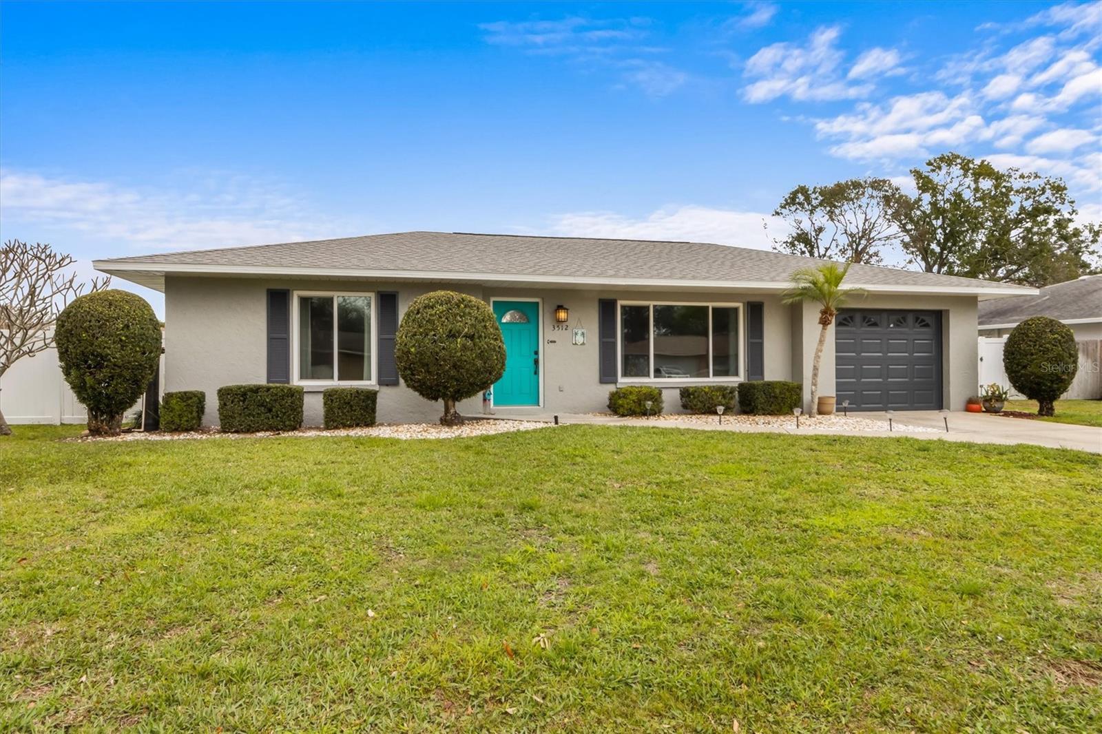 Single-story home with a turquoise front door, dark garage door, and neatly trimmed front lawn.